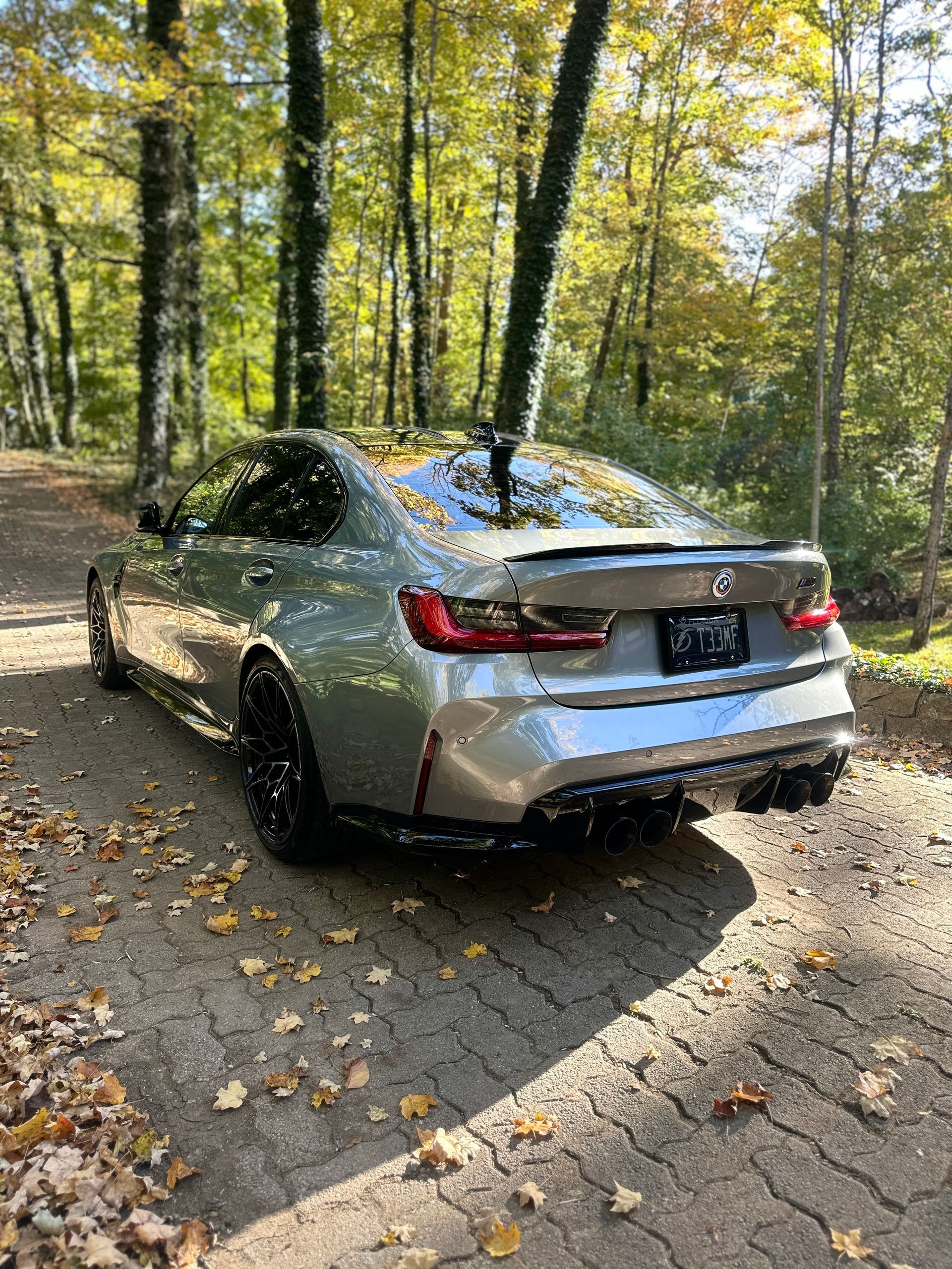 Silver BMW sedan parked on a dirt road in a forest during autumn.