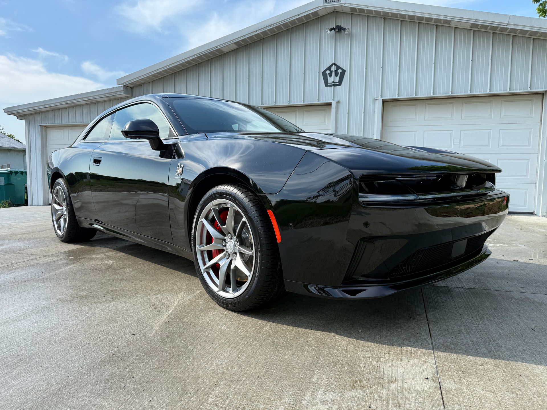 Black Dodge Charger coupe parked in front of a white garage on a sunny day.