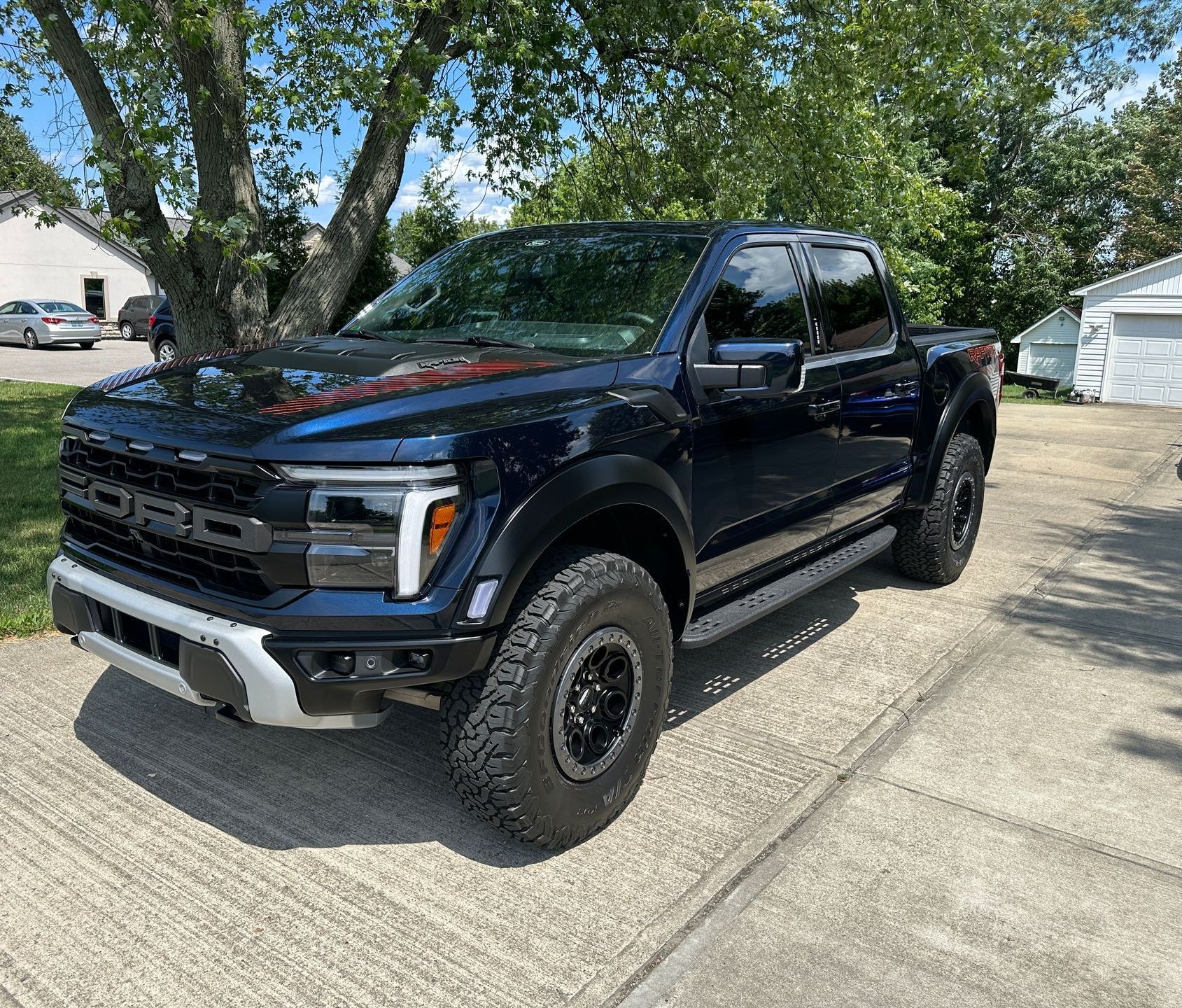 Blue Ford Raptor truck parked on a driveway, daytime.