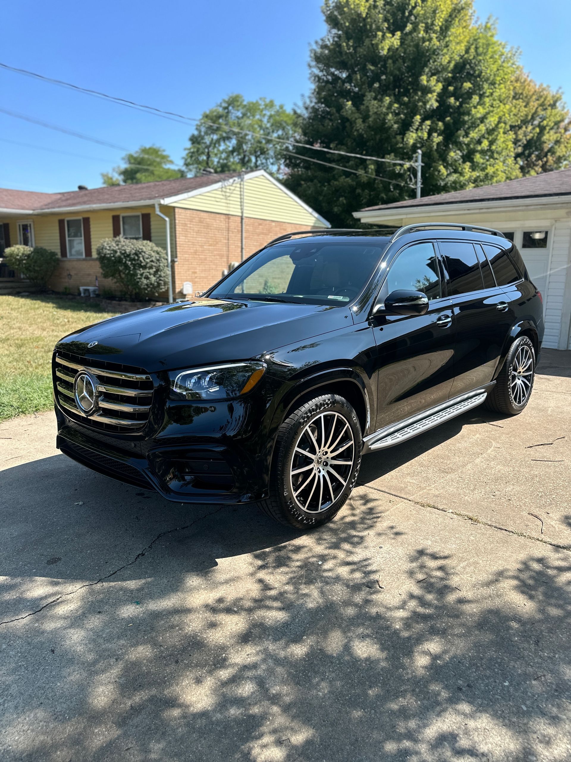 Black Mercedes-Benz SUV parked on a driveway, with a house and trees in the background on a sunny day.