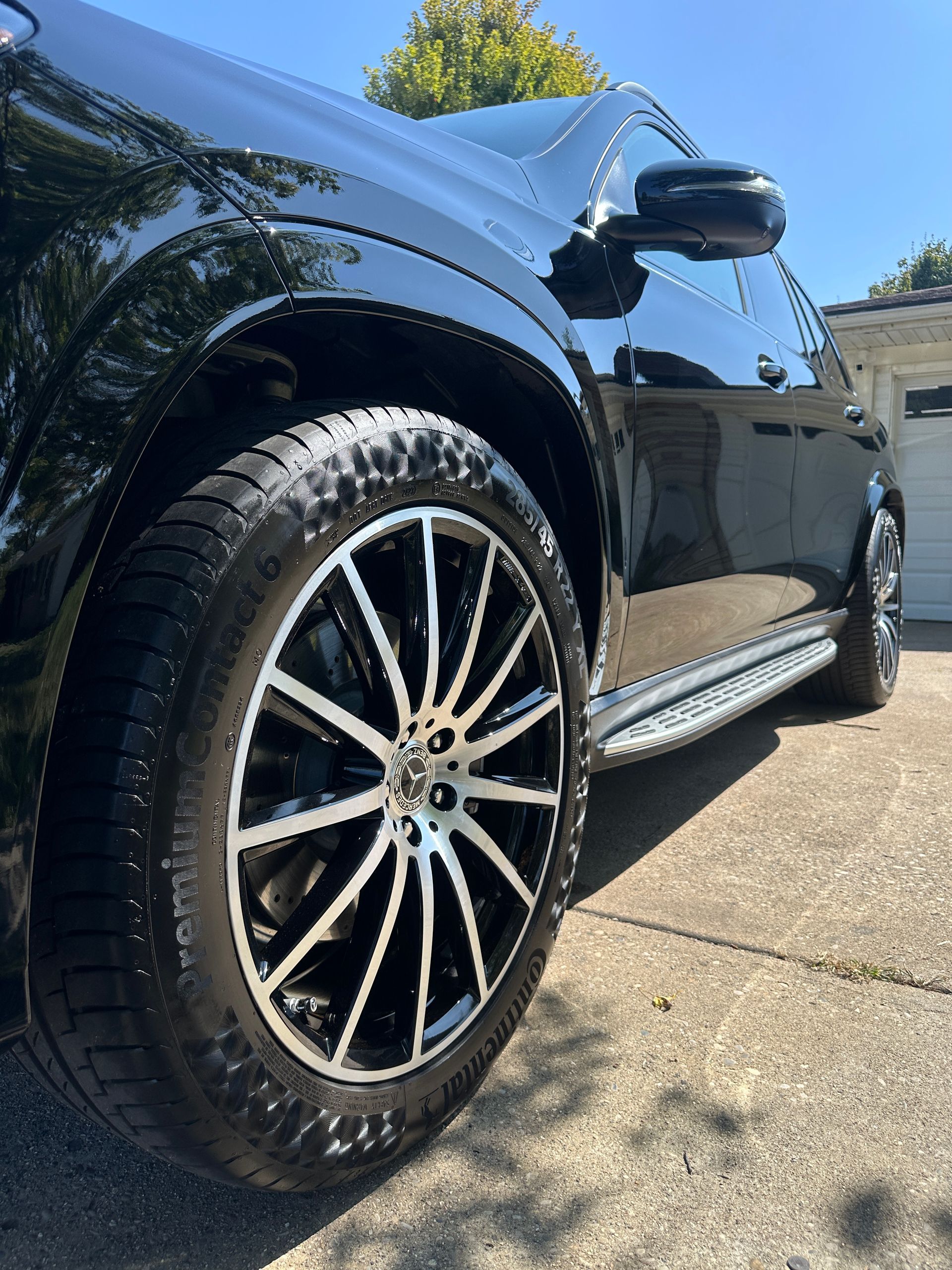Close-up of a shiny black SUV with silver and black rims, parked on a concrete driveway.