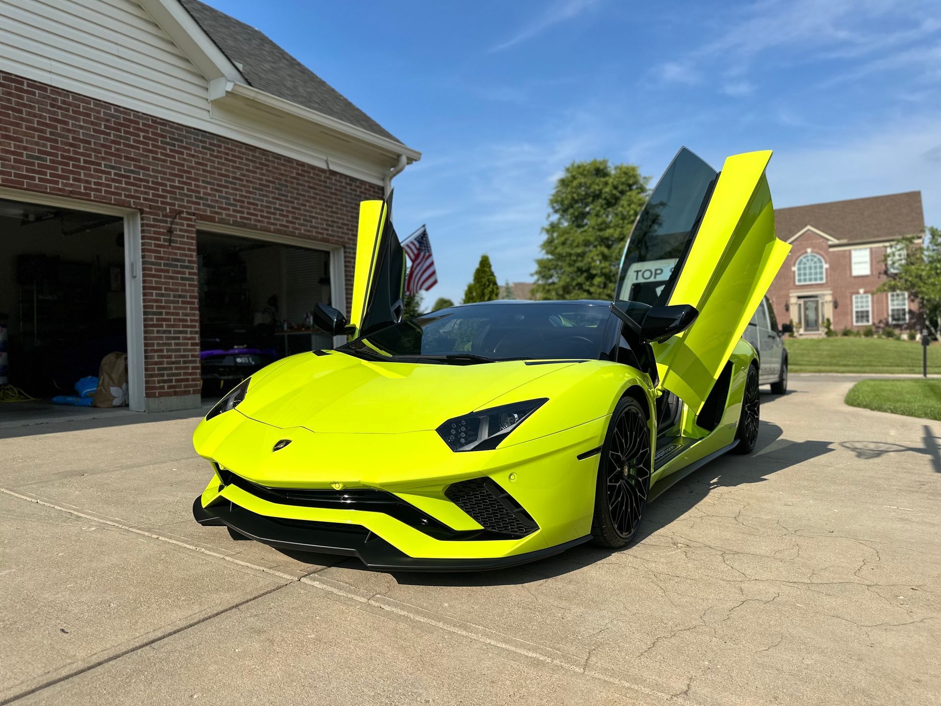 A bright yellow lamborghini aventador is parked in front of a garage with its doors open.