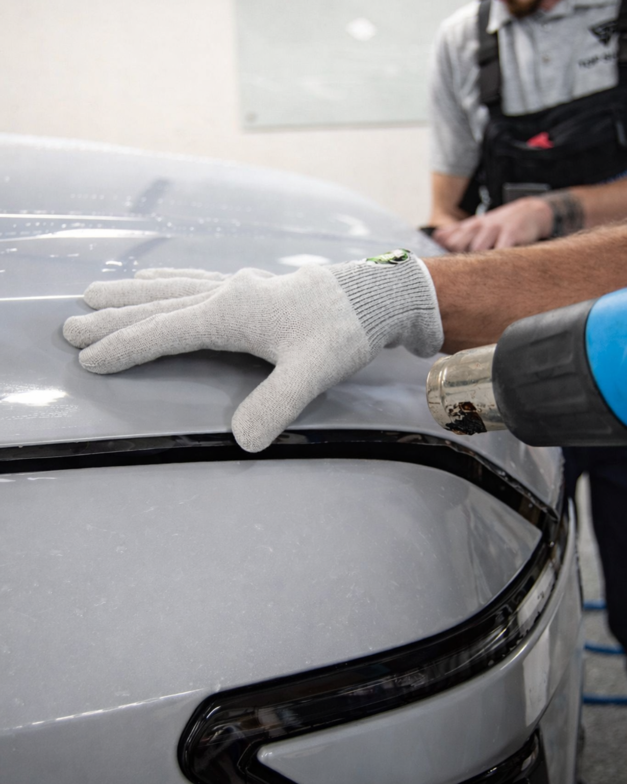 A person wearing black gloves is polishing a black car