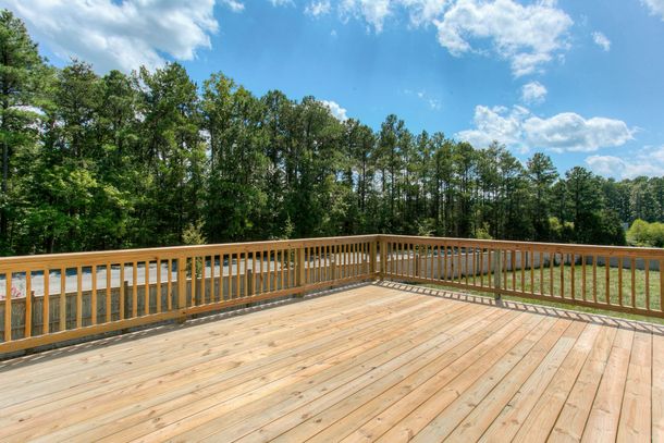 Wooden deck with railings overlooking trees under a blue sky with clouds