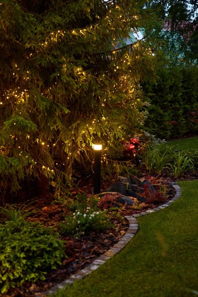 Curved garden path with brick edging, lush plants, and warm path lights at dusk