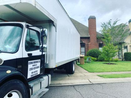 Moving truck parked in front of a house, white and black colors, green lawn.