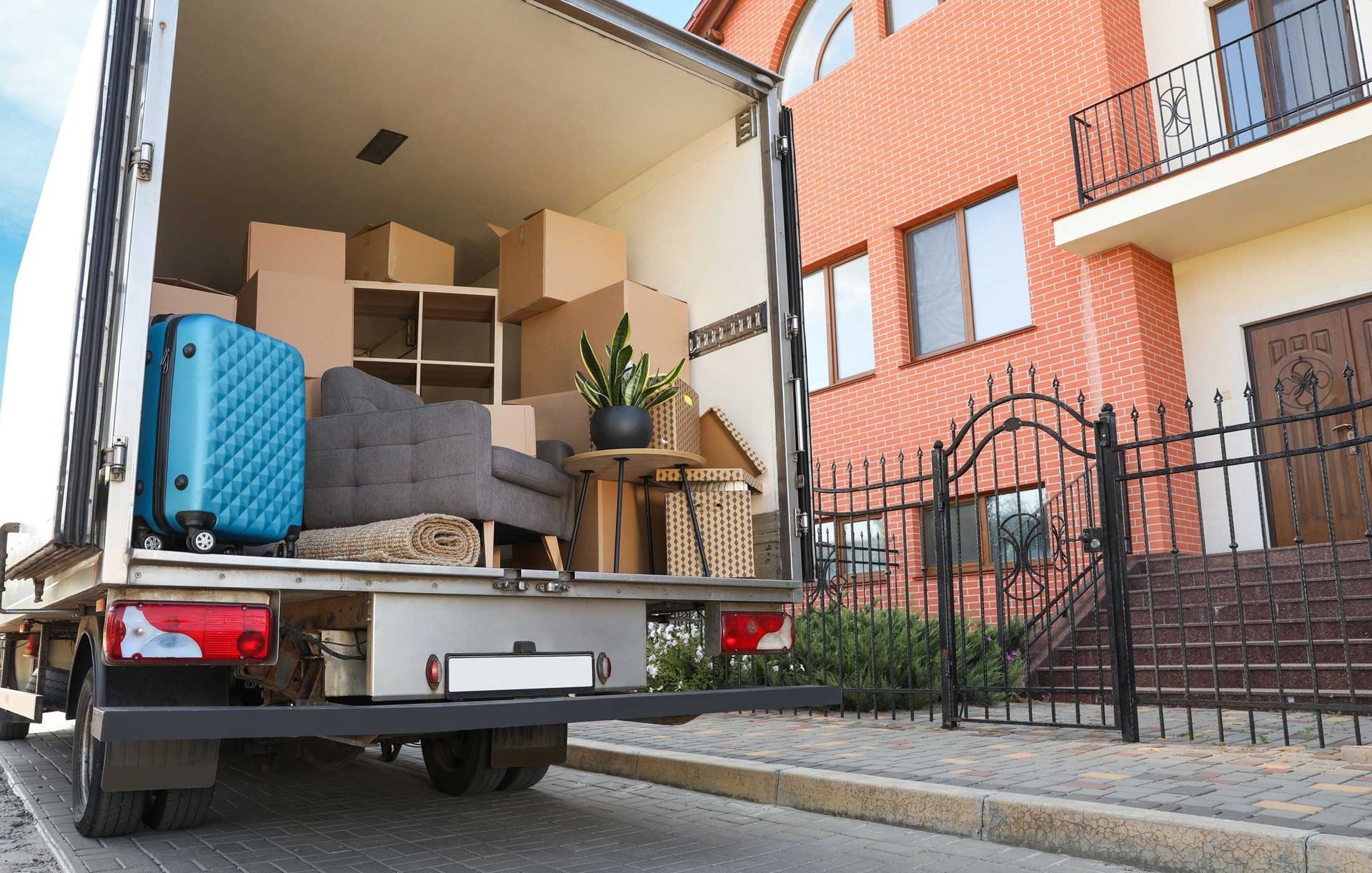 Moving truck loaded with furniture and boxes in front of a brick house.