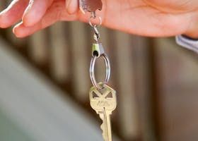 Hand holding a key, attached to a metal loop and clasp, in front of a blurred background.
