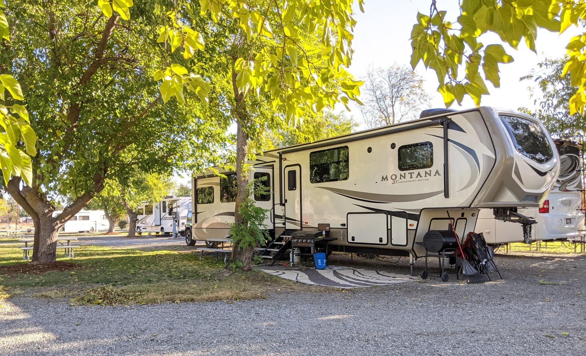 A rv is parked in a gravel lot next to a tree.