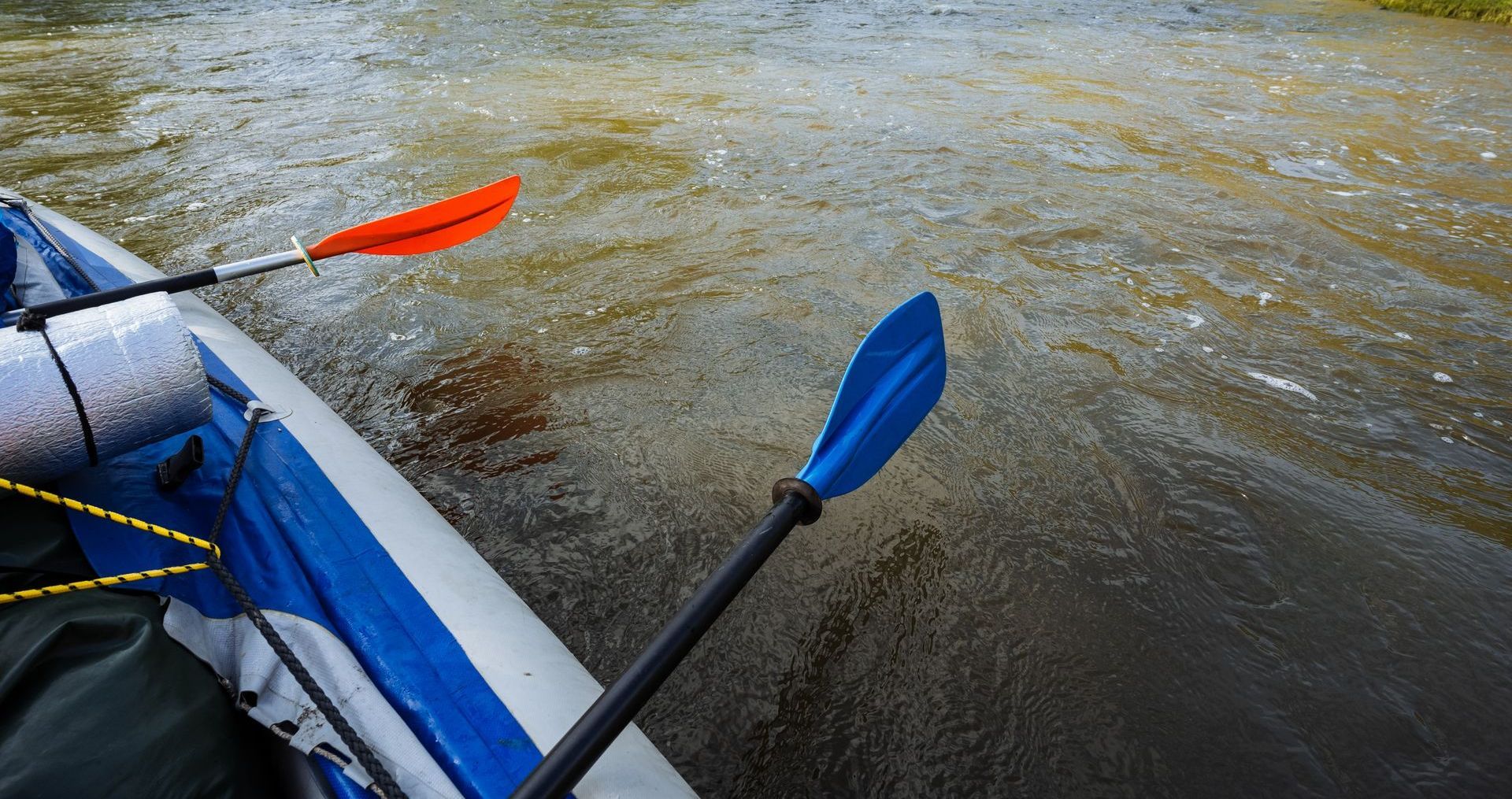 A kayak is floating down a river with two paddles.