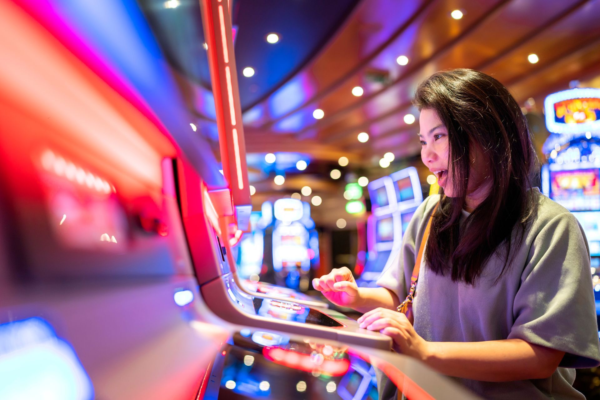 Woman playing a slot machine, illuminated by bright casino lights, showing an excited expression.