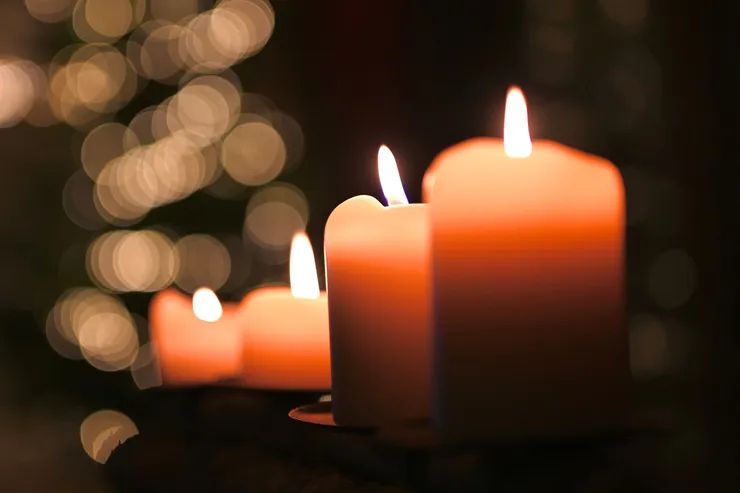 Quattro candele arancioni accese in fila con luci sfocate sullo sfondo.