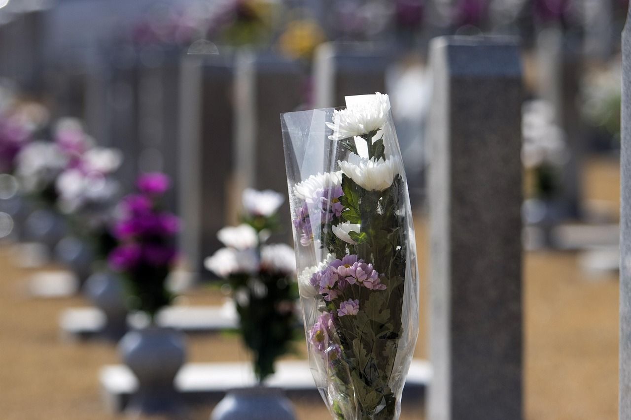 Fiori avvolti nella plastica davanti a una fila di lapidi in un cimitero.