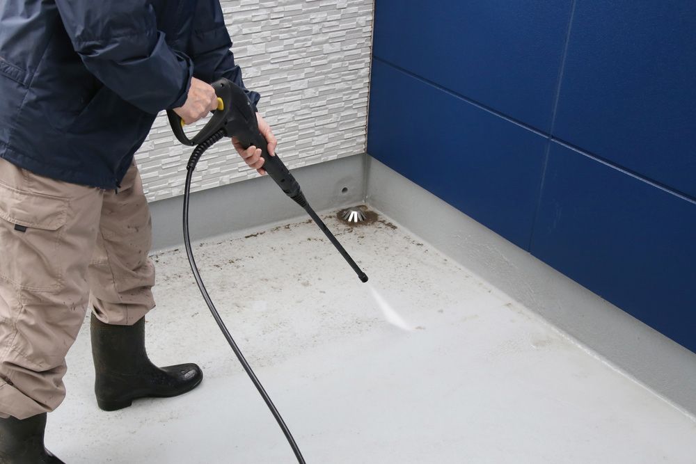 A Man is Cleaning the Floor With a High Pressure Washer — Ryno's Plumbing Group in Forster, NSW