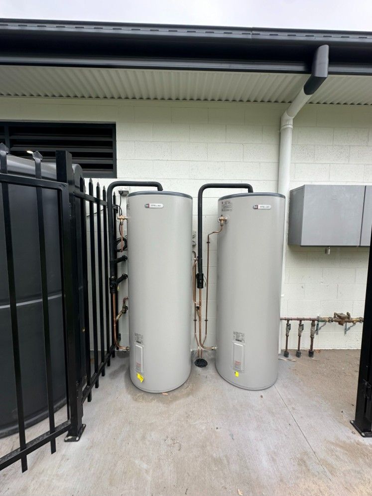 Two Water Heaters Are Sitting Outside of a Building Next to a Black Fence — Ryno's Plumbing Group in Laurieton, NSW