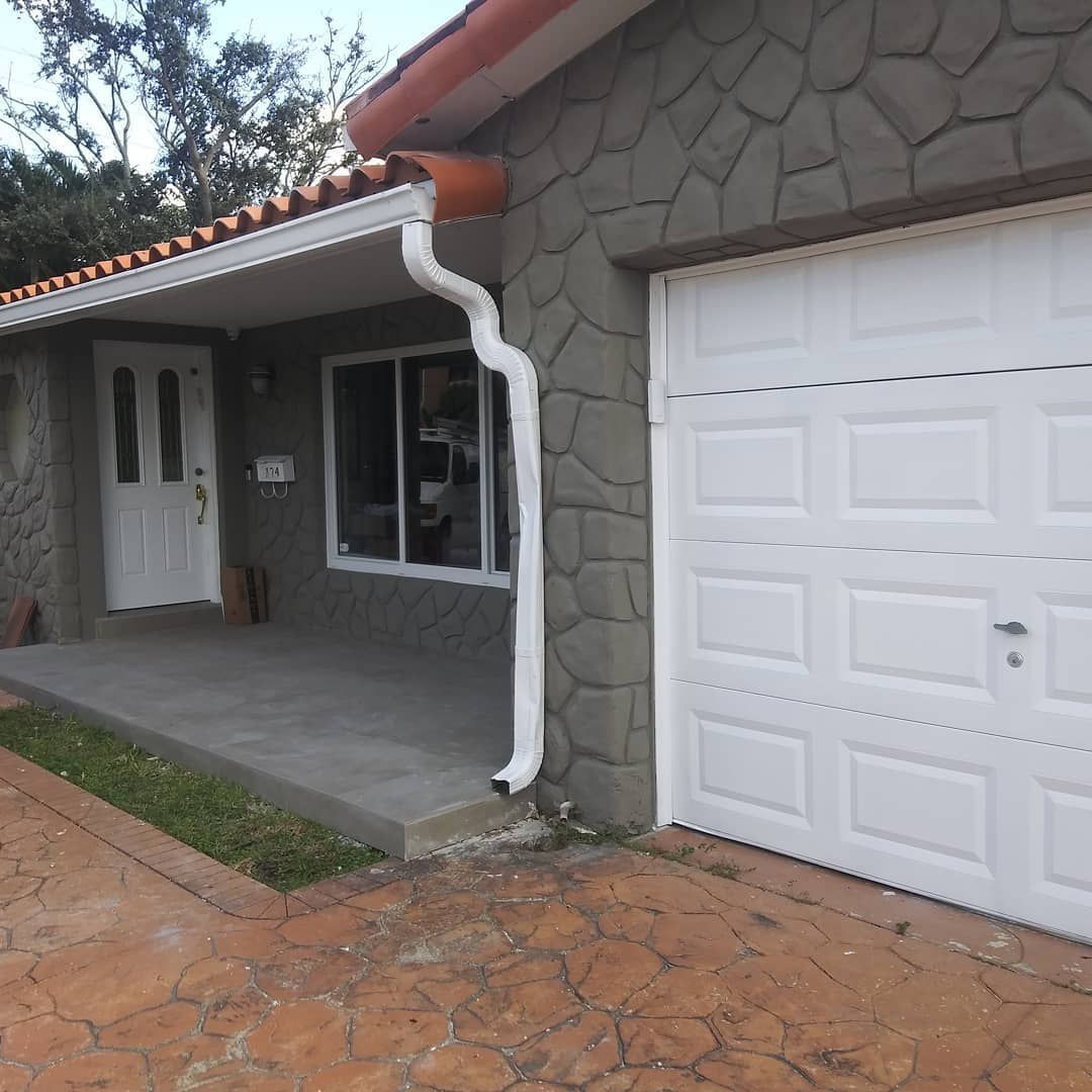 A white garage door is next to a stone house