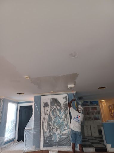 A man is painting the ceiling of a living room with a roller.