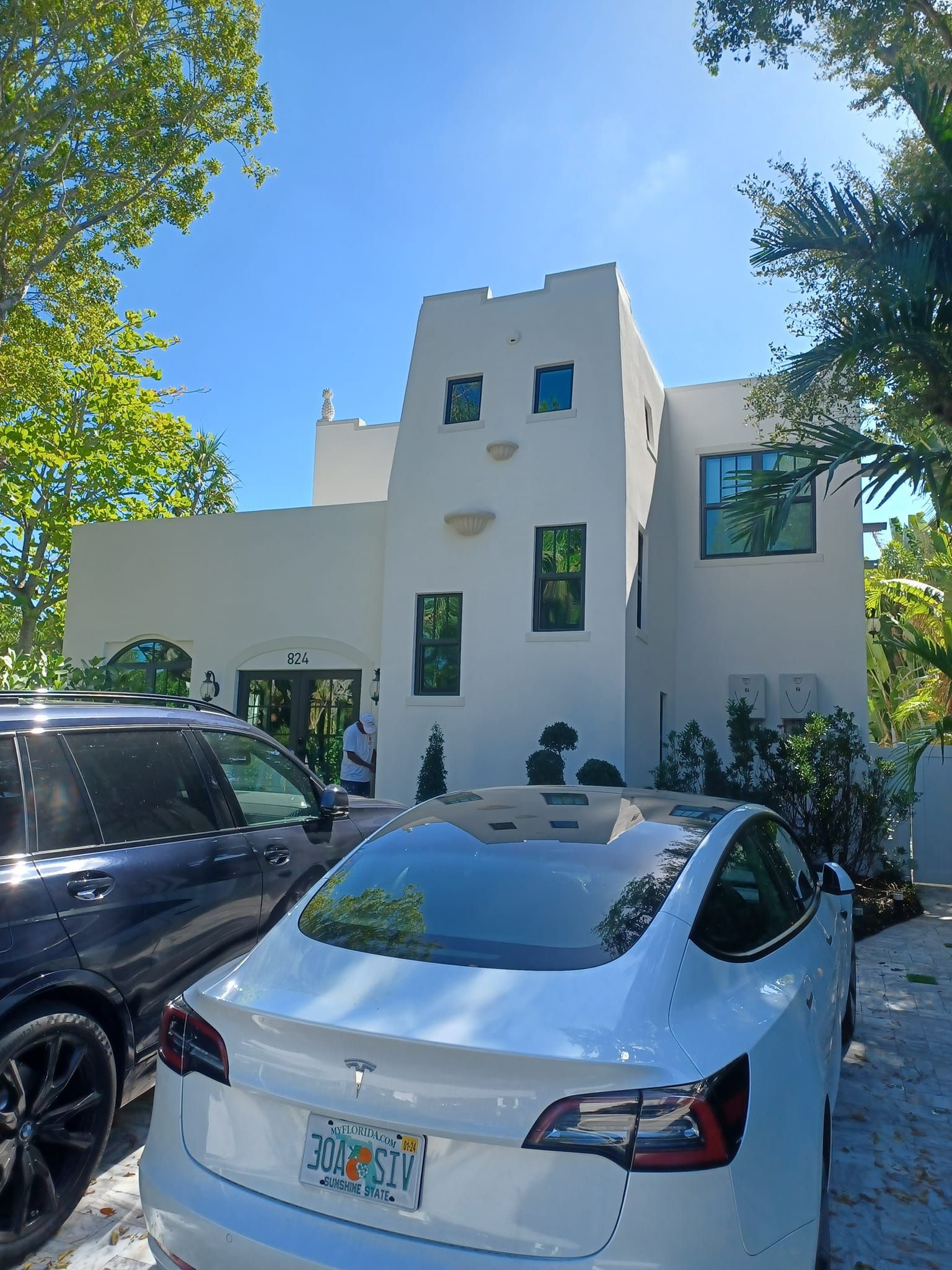 A white tesla model 3 is parked in front of a white house.