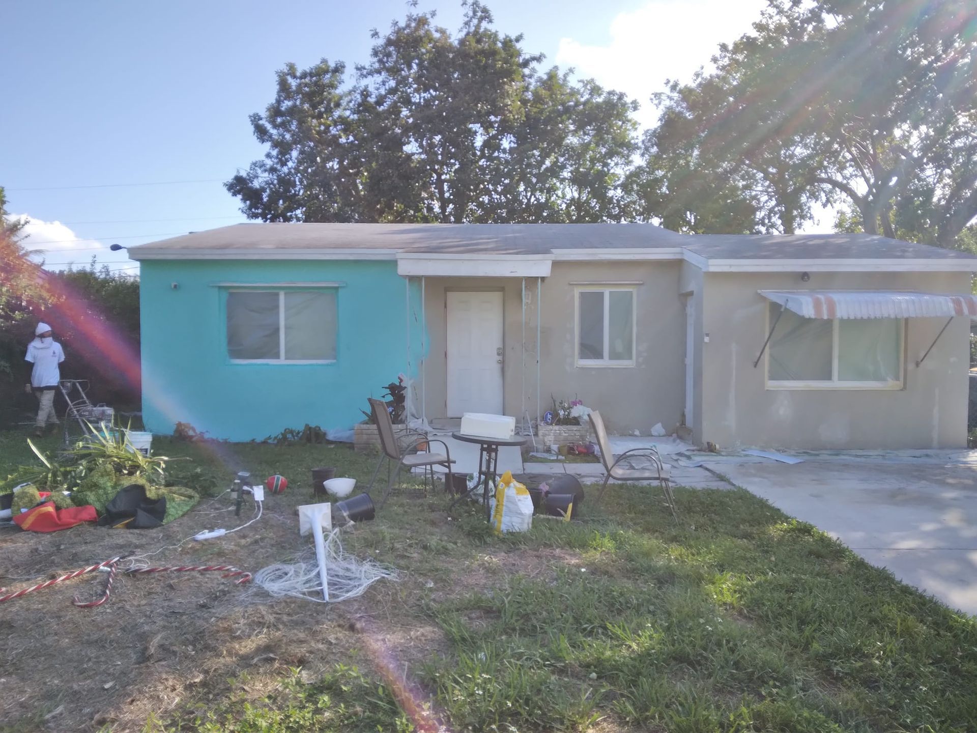 A house is being painted blue and gray and a man is standing in front of it.