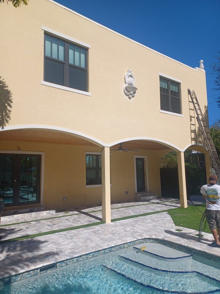 A man is painting the outside of a house next to a pool.