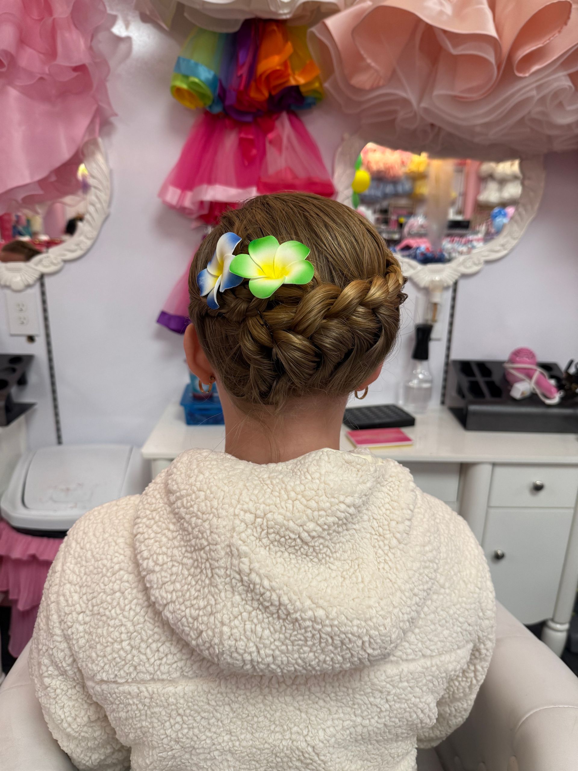 A little girl is wearing a braided bun with flowers in her hair.