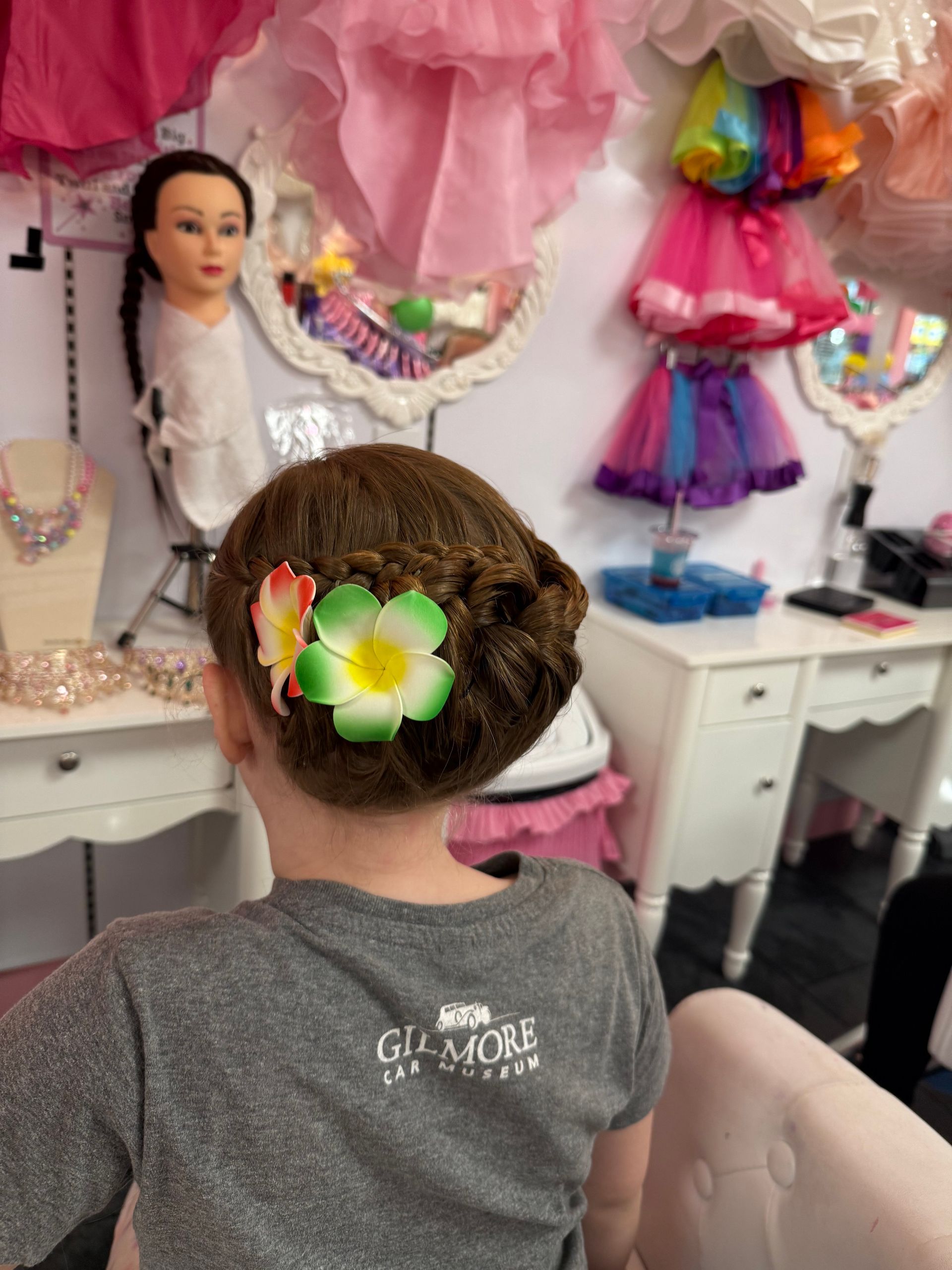 A little girl is sitting in a chair with a flower in her hair.