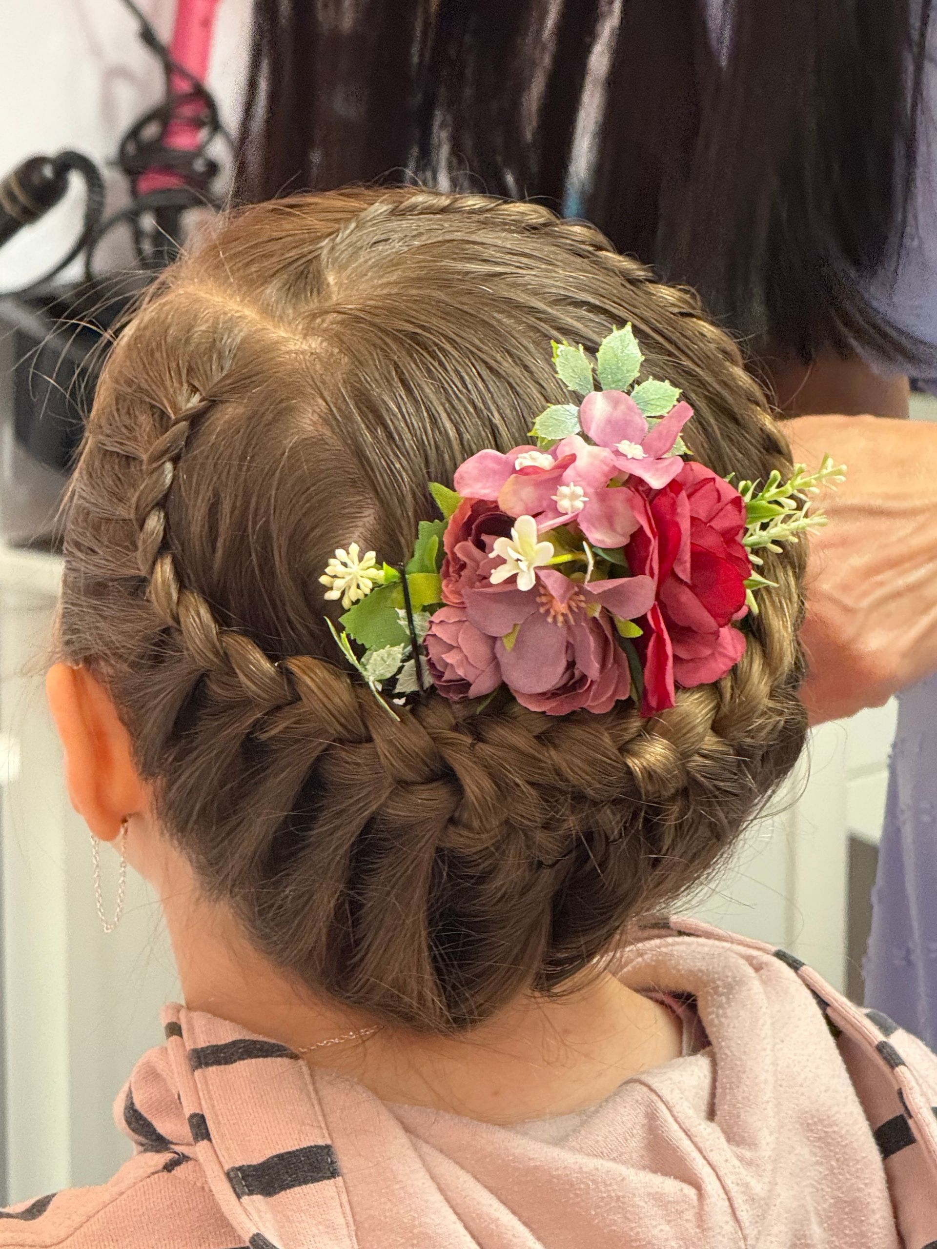 A little girl is getting her hair done by a hairdresser with flowers in her hair.