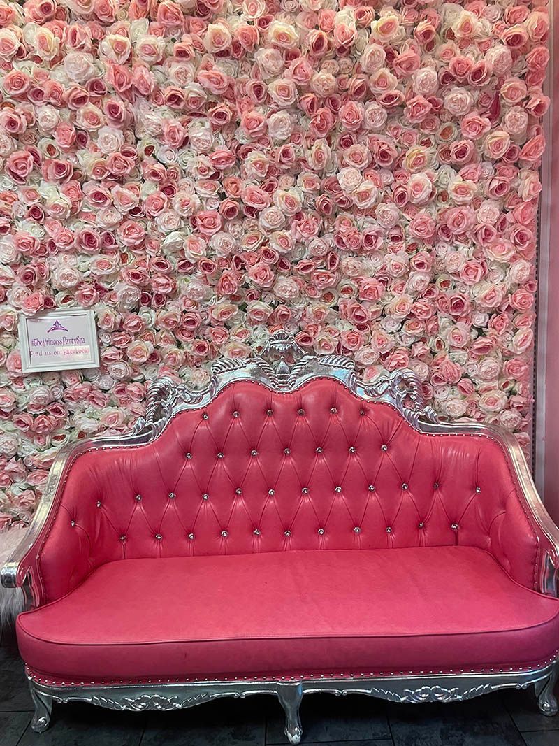A pink couch is sitting in front of a wall of pink flowers.