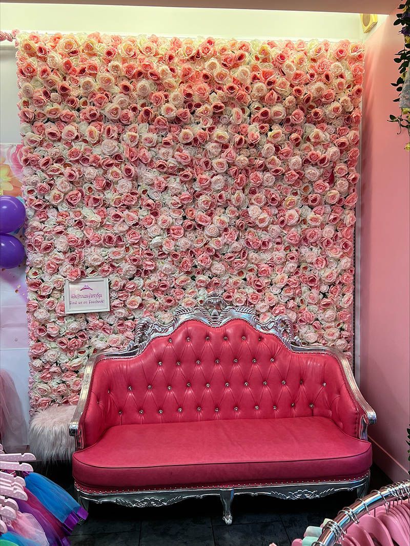 A pink couch is sitting in front of a wall of pink flowers.
