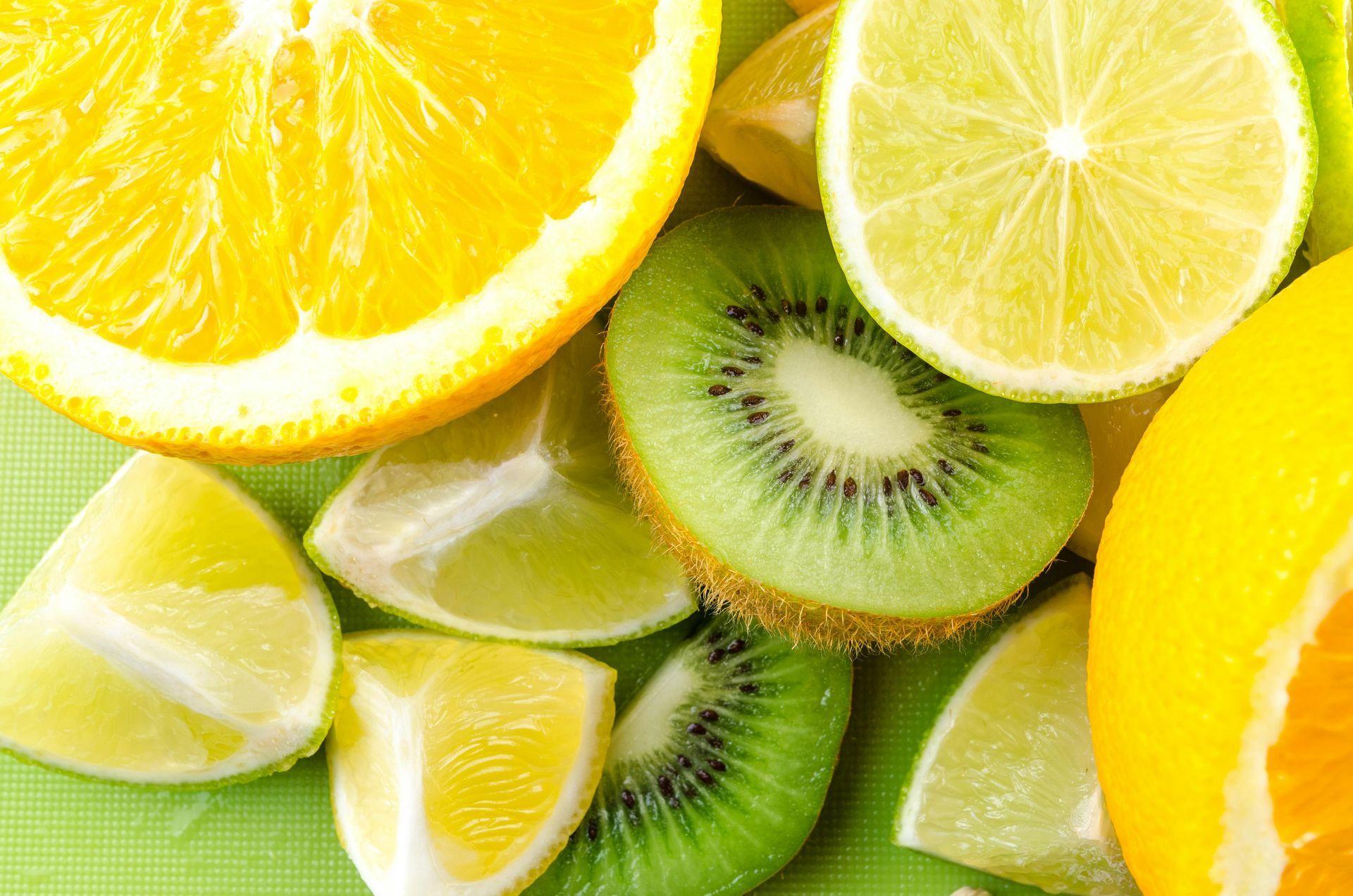 Sliced citrus fruit, including orange, lime, and lemon, with kiwi on a green surface.