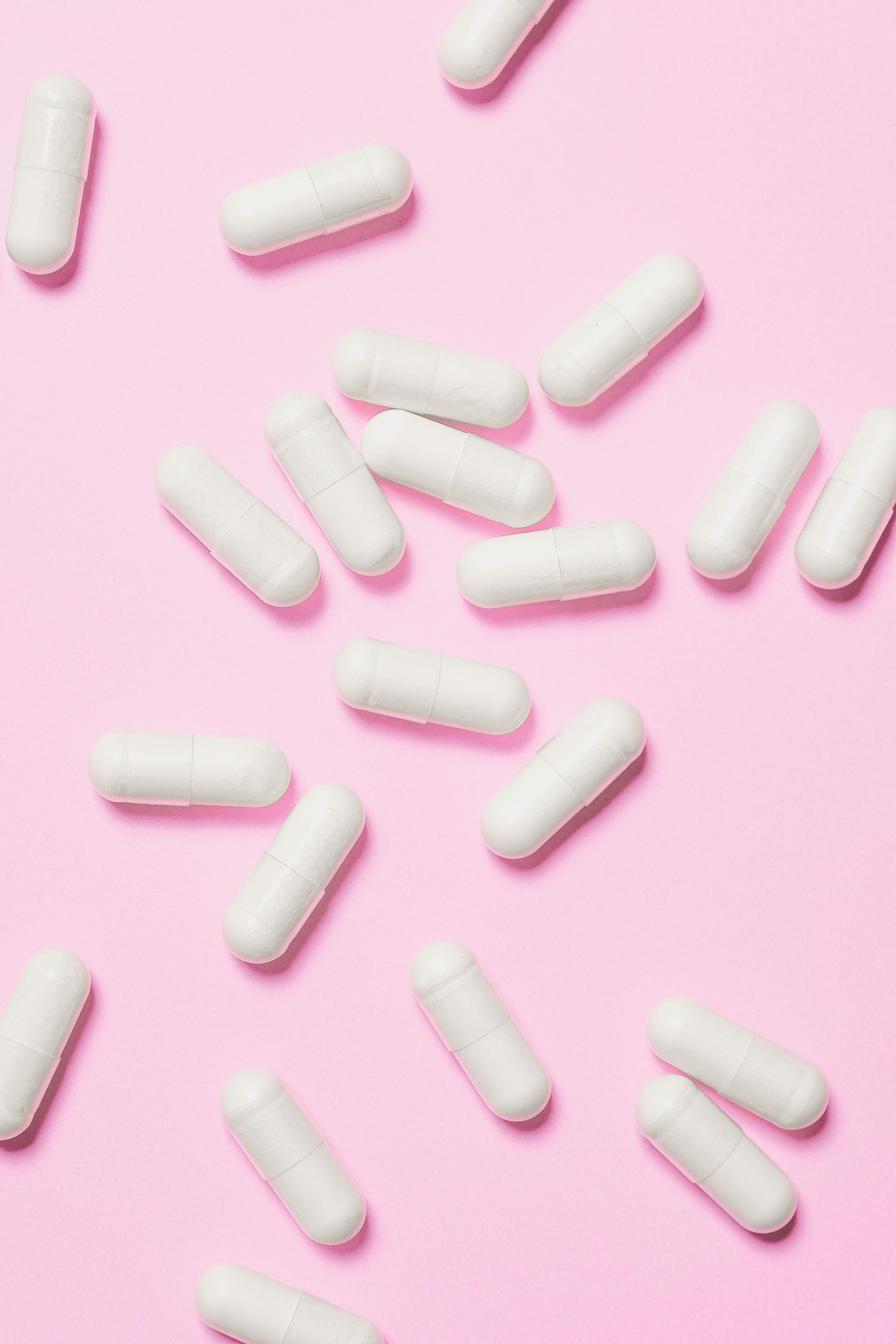 White capsule pills scattered on a pink background.