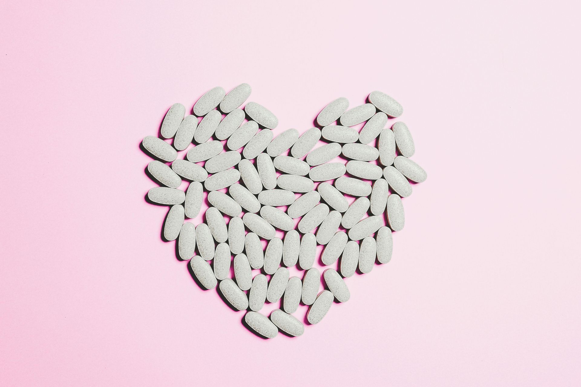 White pills arranged in a heart shape on a pink background.