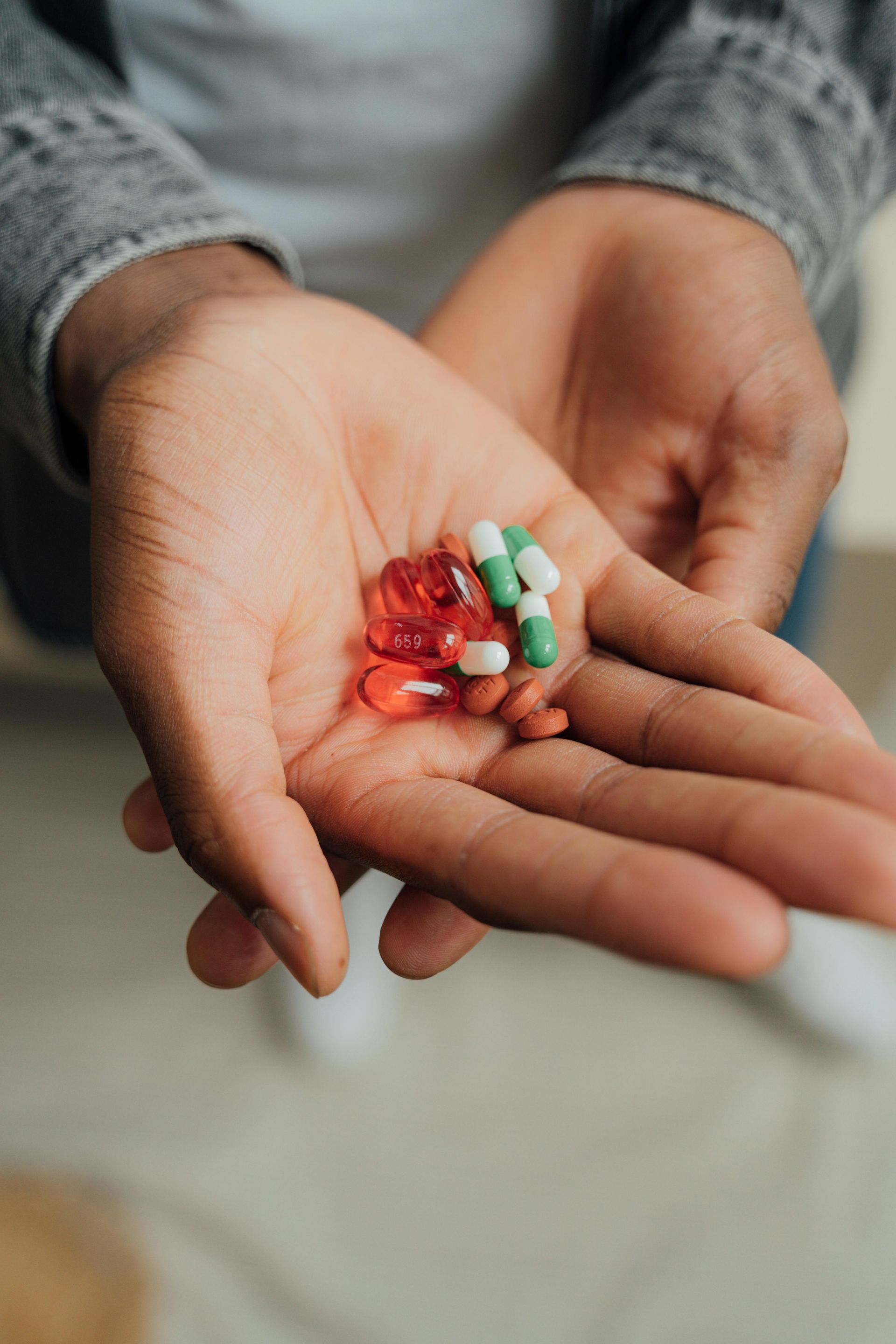Person holding a handful of pills in their open palms; red and green capsules are visible.
