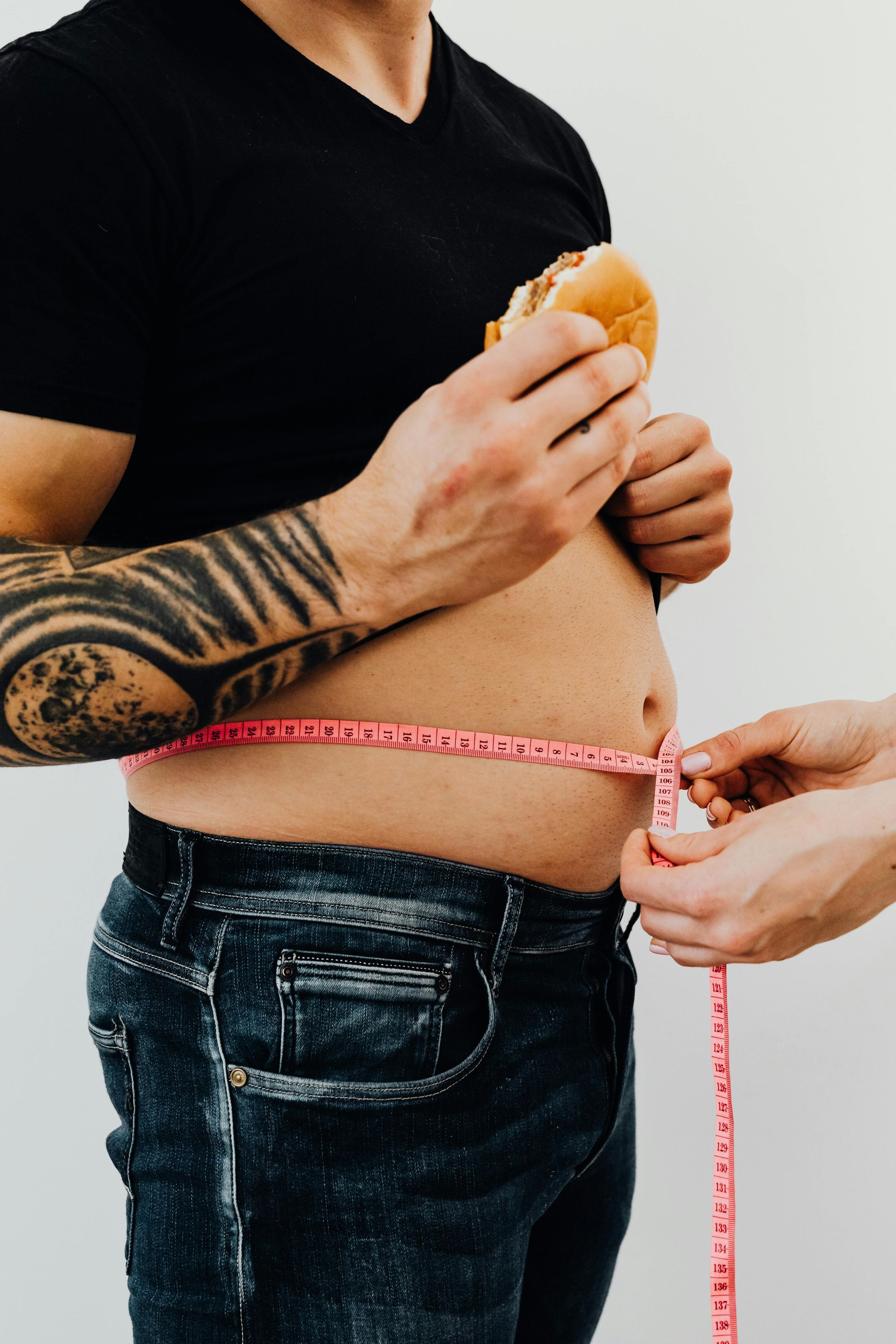 Person holding a hamburger, waist being measured with a pink tape.