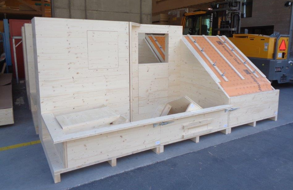 Eine grosse Holzkiste steht auf dem Boden vor einem Gabelstapler