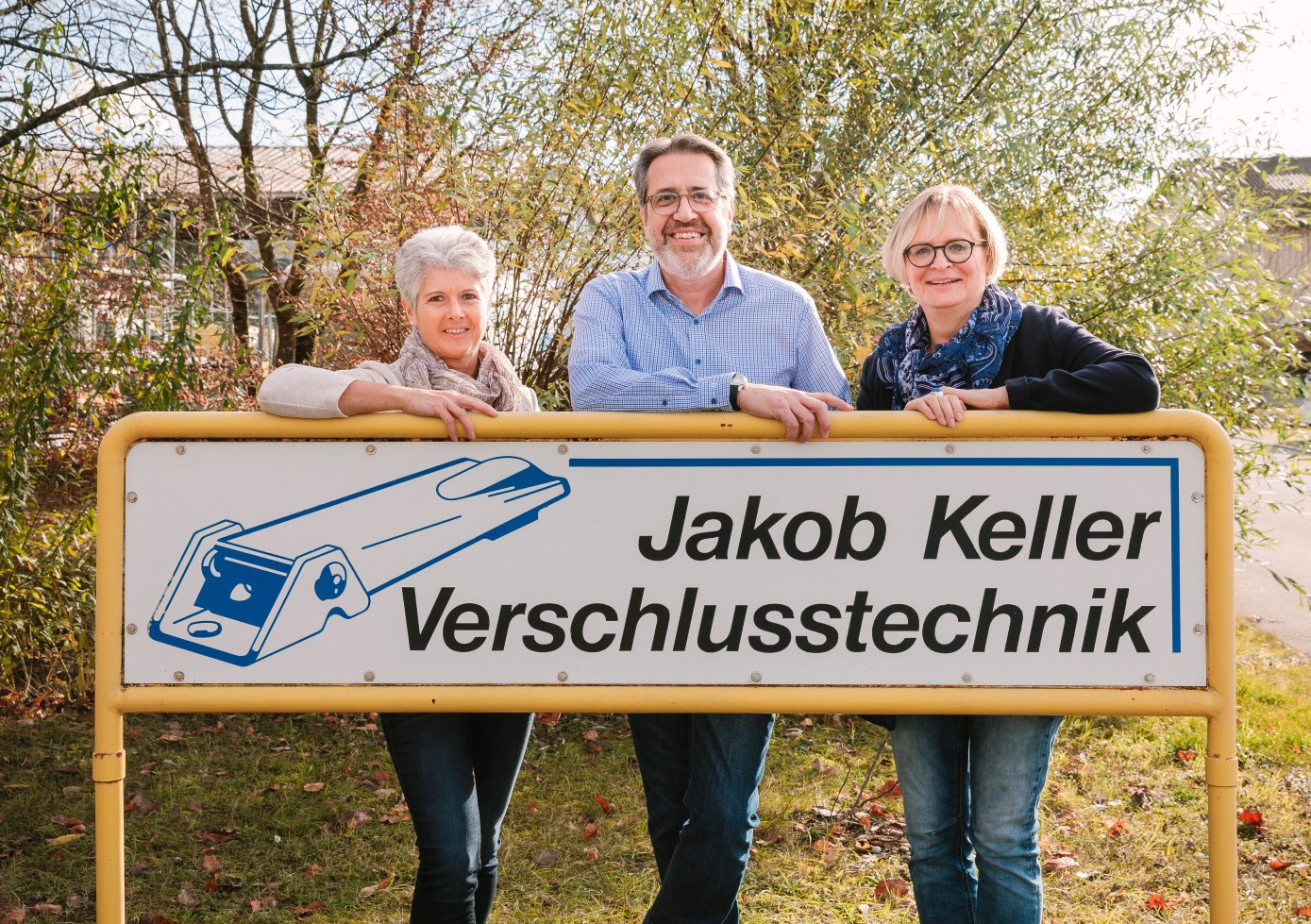 Eine Gruppe von Menschen steht hinter einem Schild mit der Aufschrift „Jakob Keller“