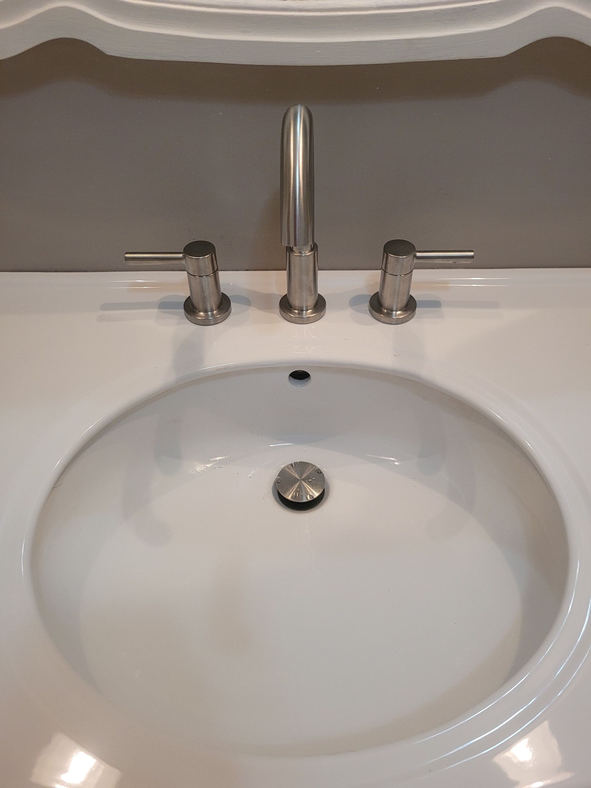 White bathroom sink with three-piece brushed nickel faucet set. Gray wall above the sink.