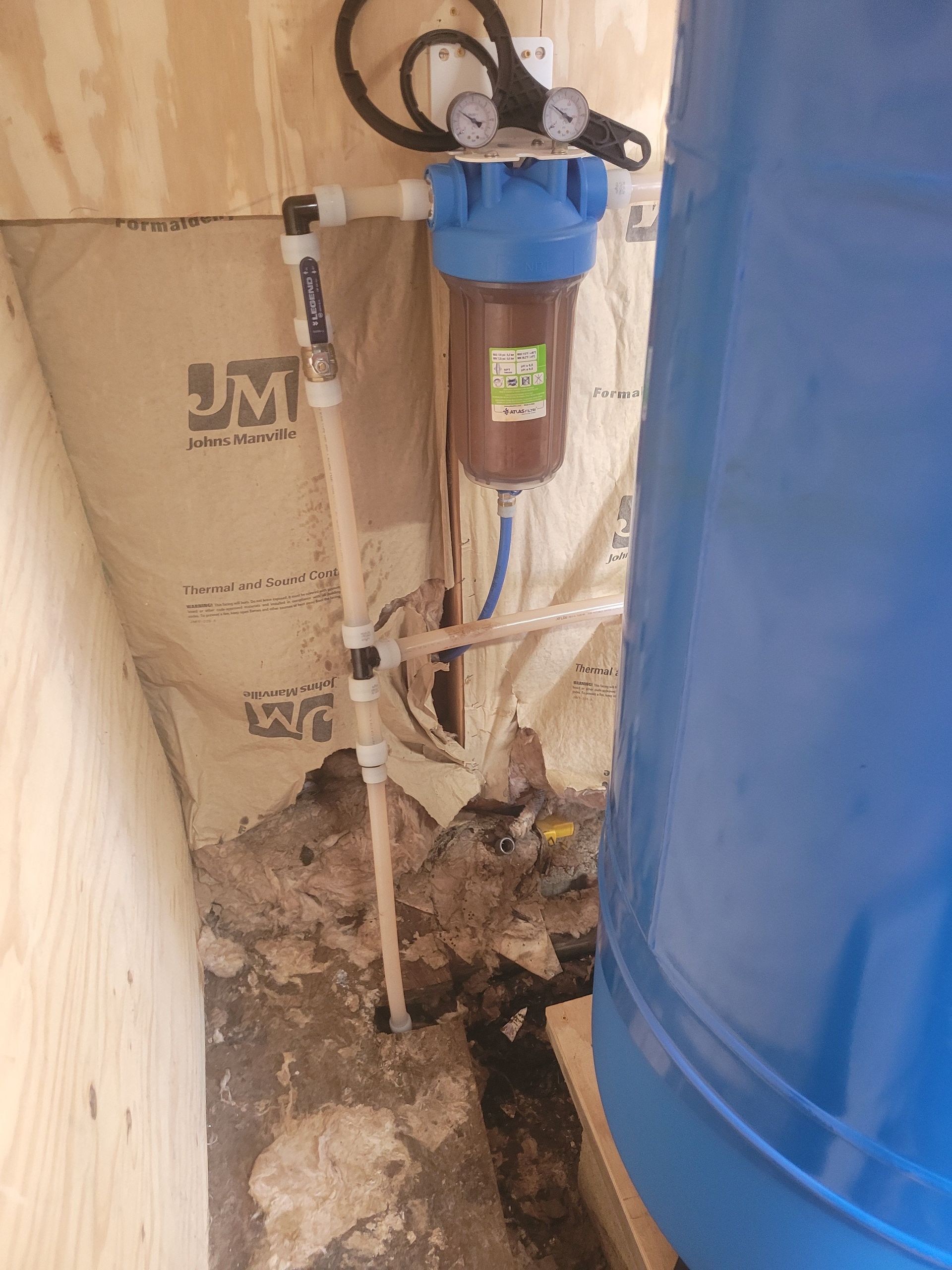Water filtration system with blue tank, brown filter, and white pipes in a utility space.