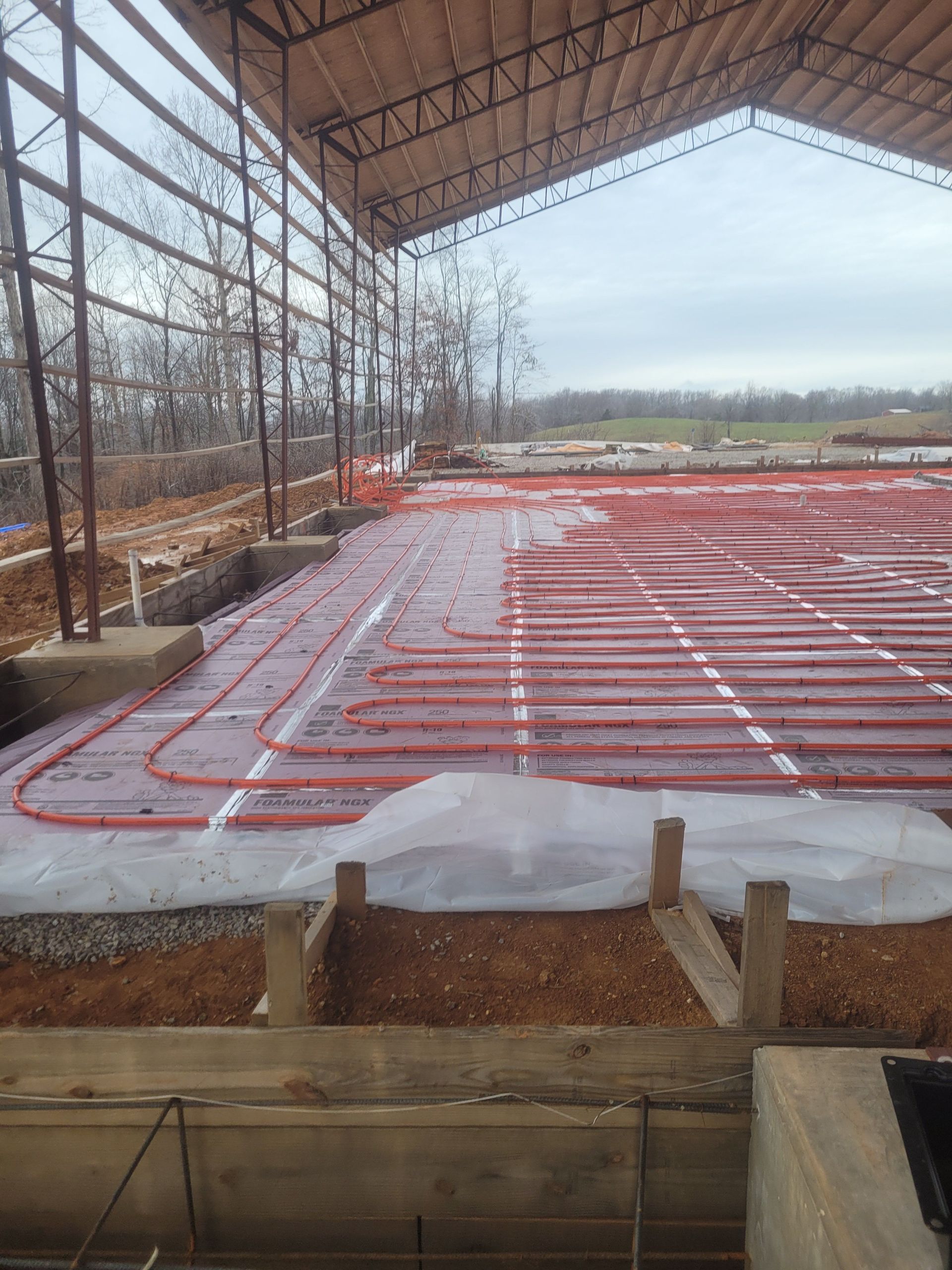 Red radiant floor heating tubes laid on a gravel base inside a partially constructed building.