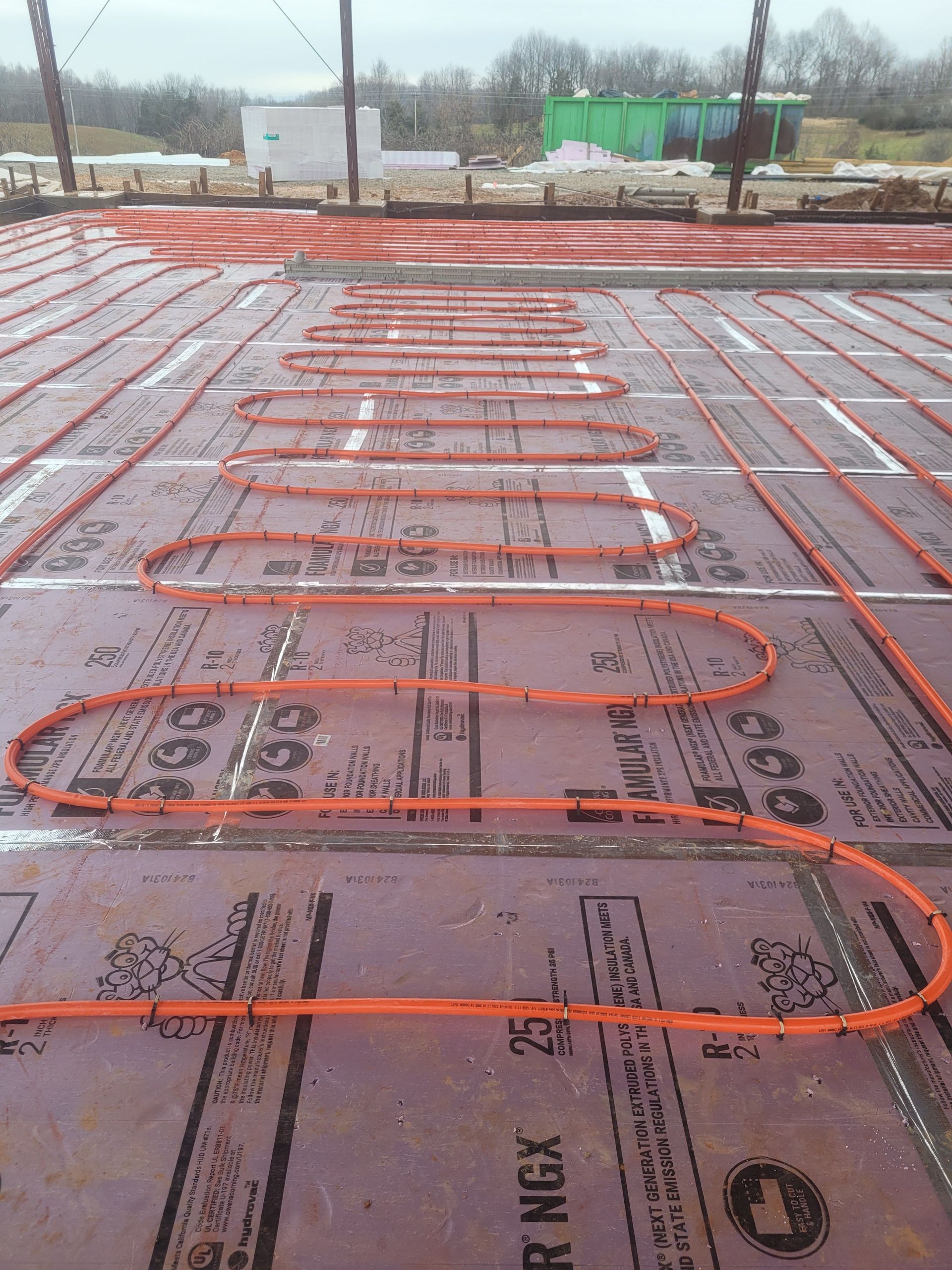 Orange tubing laid in loops on a purple insulated floor, likely for radiant heating. Outdoors, construction site.