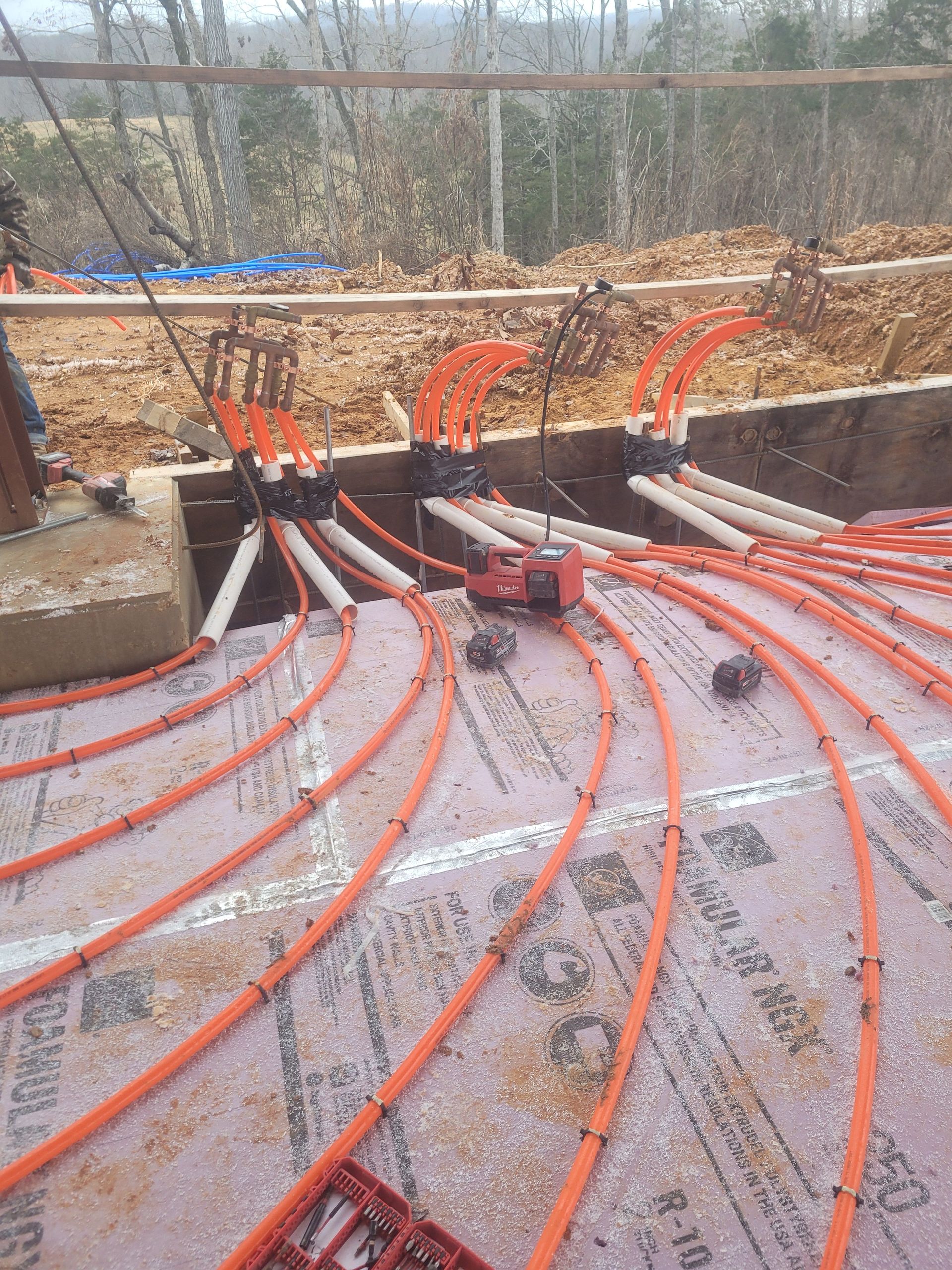 Orange radiant floor tubing installed on pink foam insulation, leading to a manifold system.