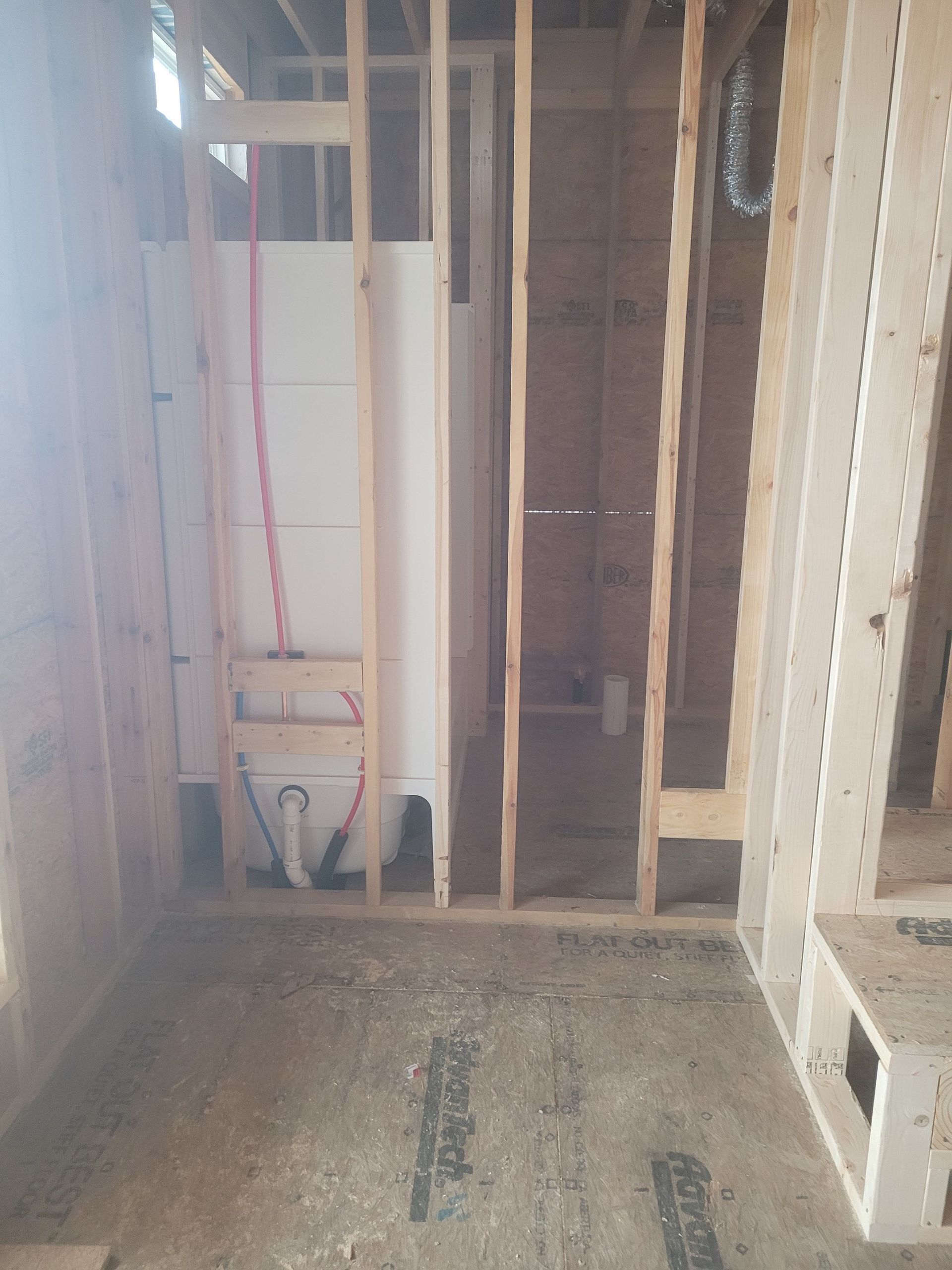 Framed walls of a bathroom under construction with a white bathtub and exposed plumbing.