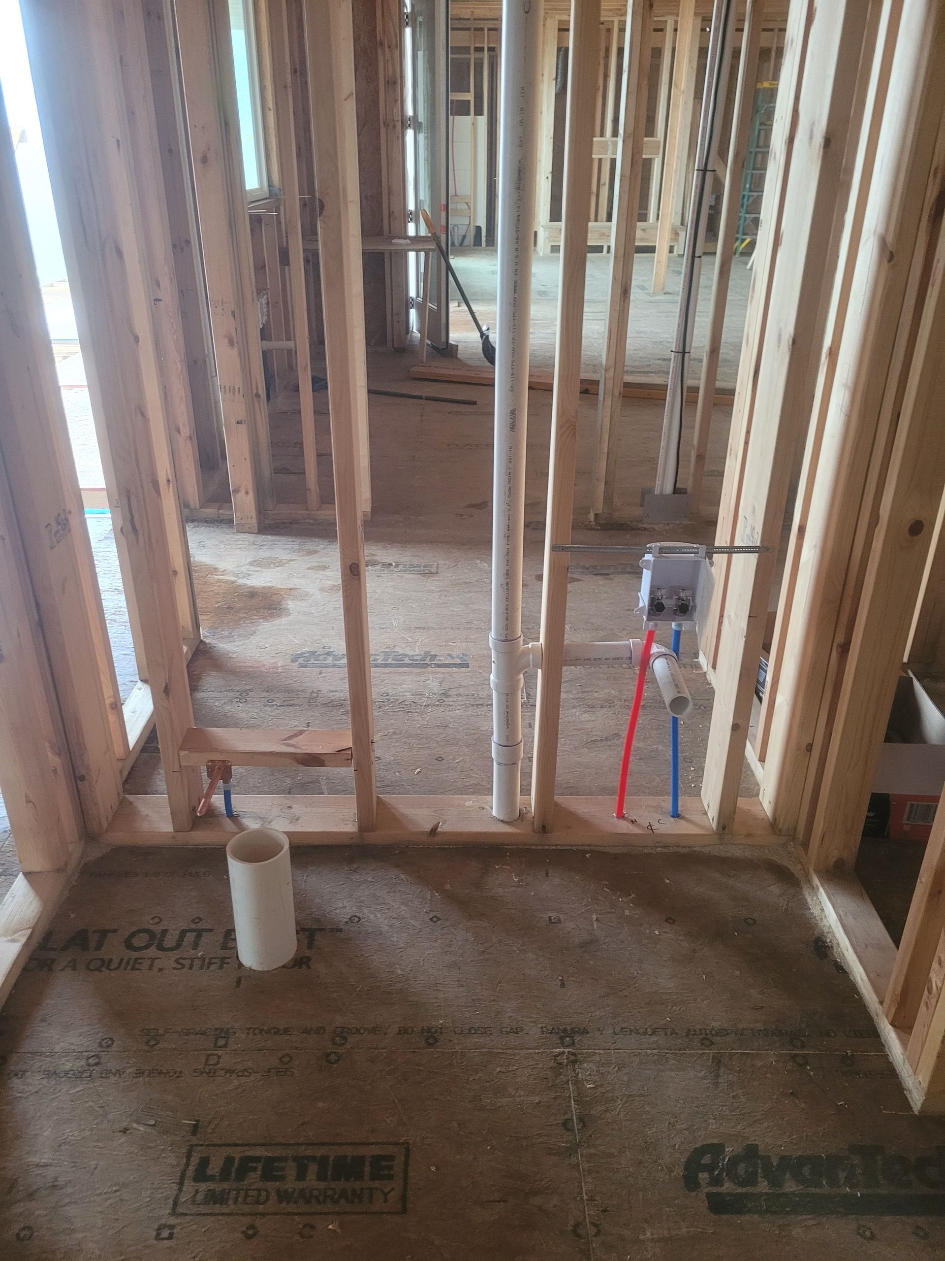 Framed interior of a building under construction. Plumbing pipes and electrical box visible within wooden framing.