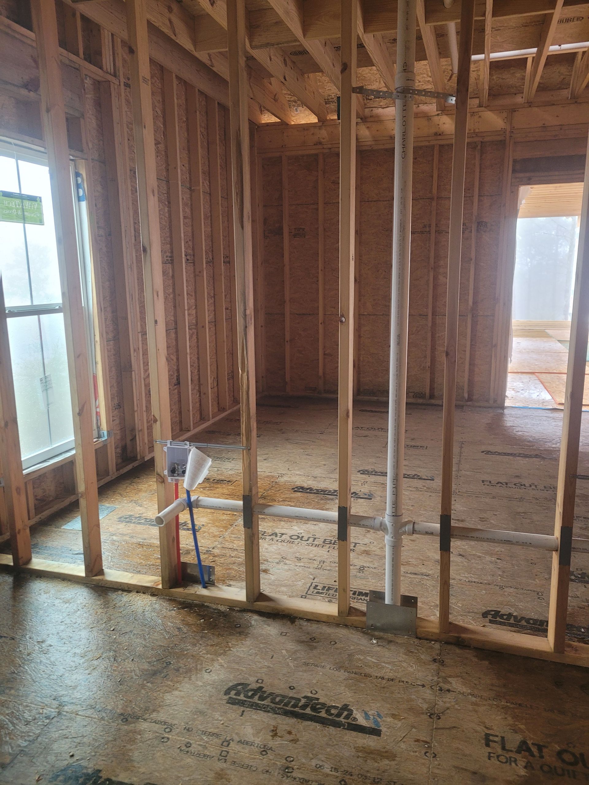 Interior of a new building under construction, showing wooden framing, plumbing, and a window.