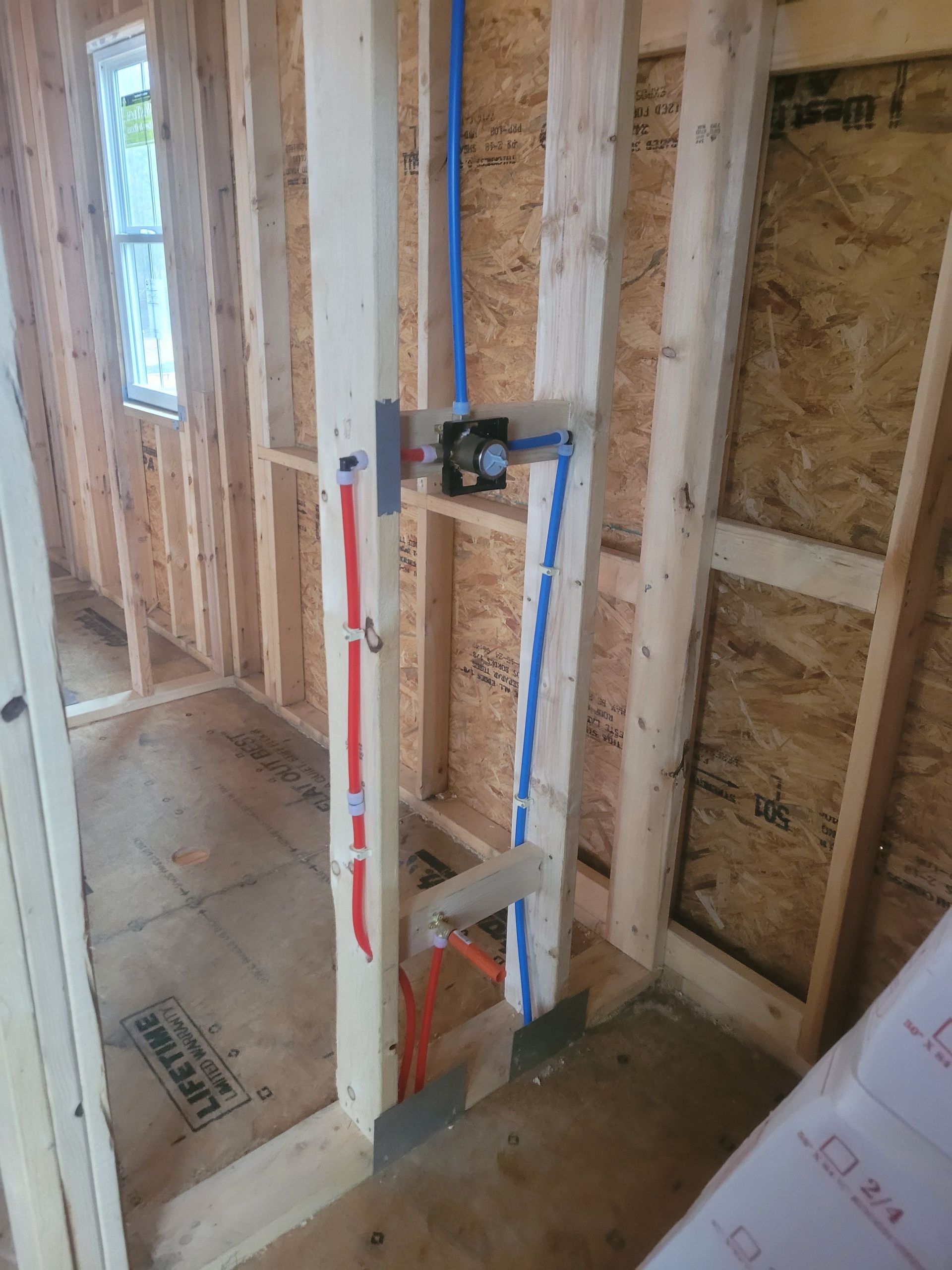Framed wall with installed plumbing for a shower. Red and blue pipes.