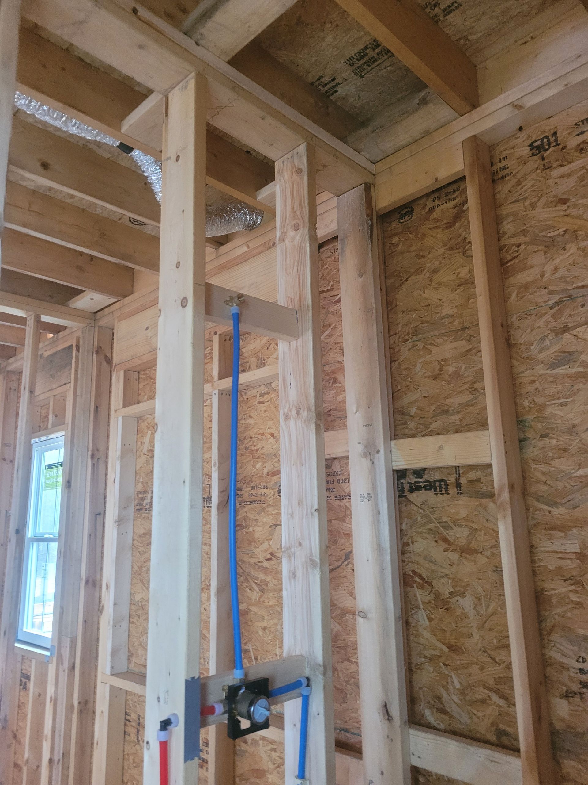 Wooden framing of a wall, with blue plumbing pipes and a shower valve installed.