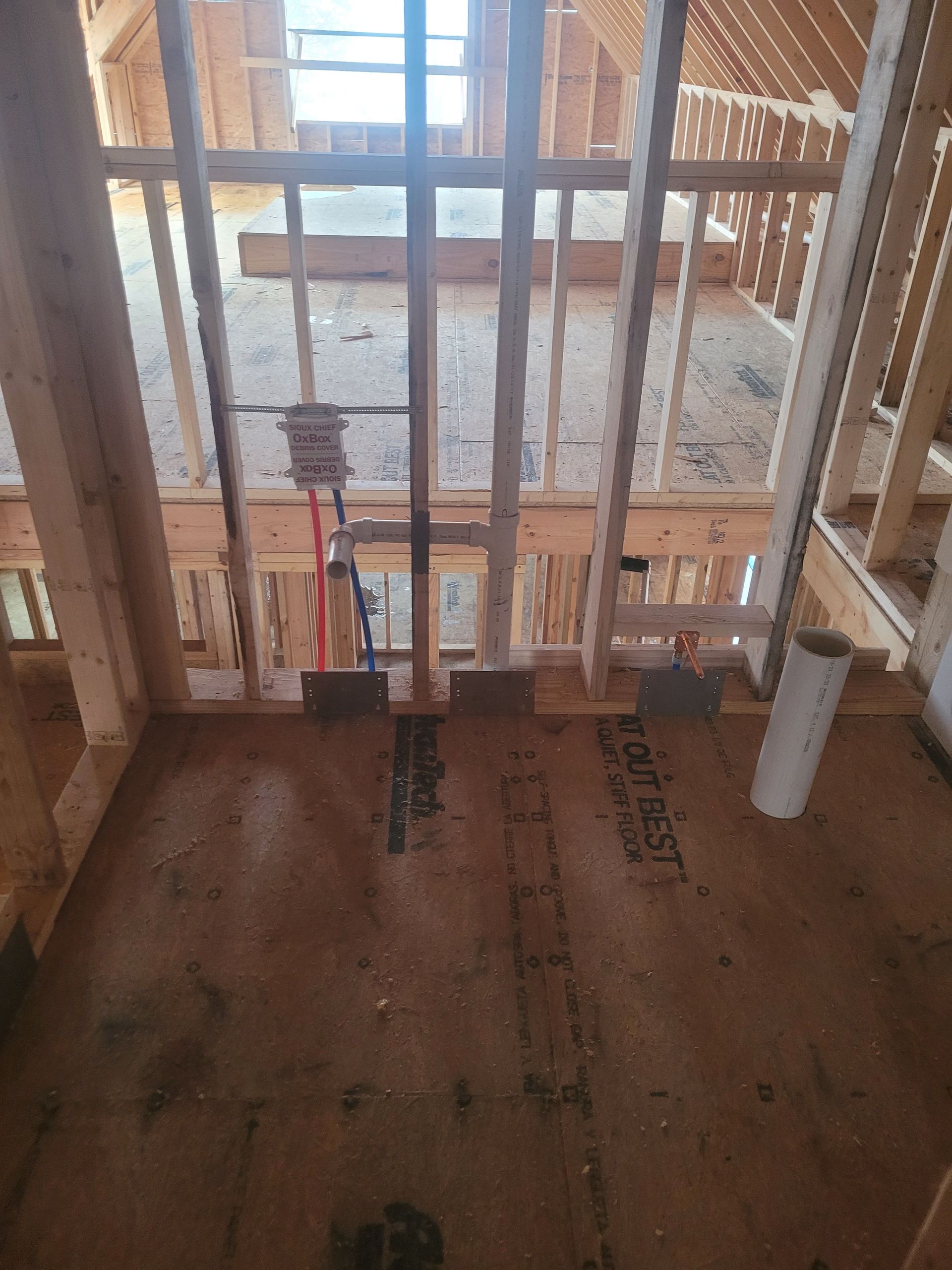 Interior view of a building under construction, showing wooden framing, plumbing, and a partially finished floor.