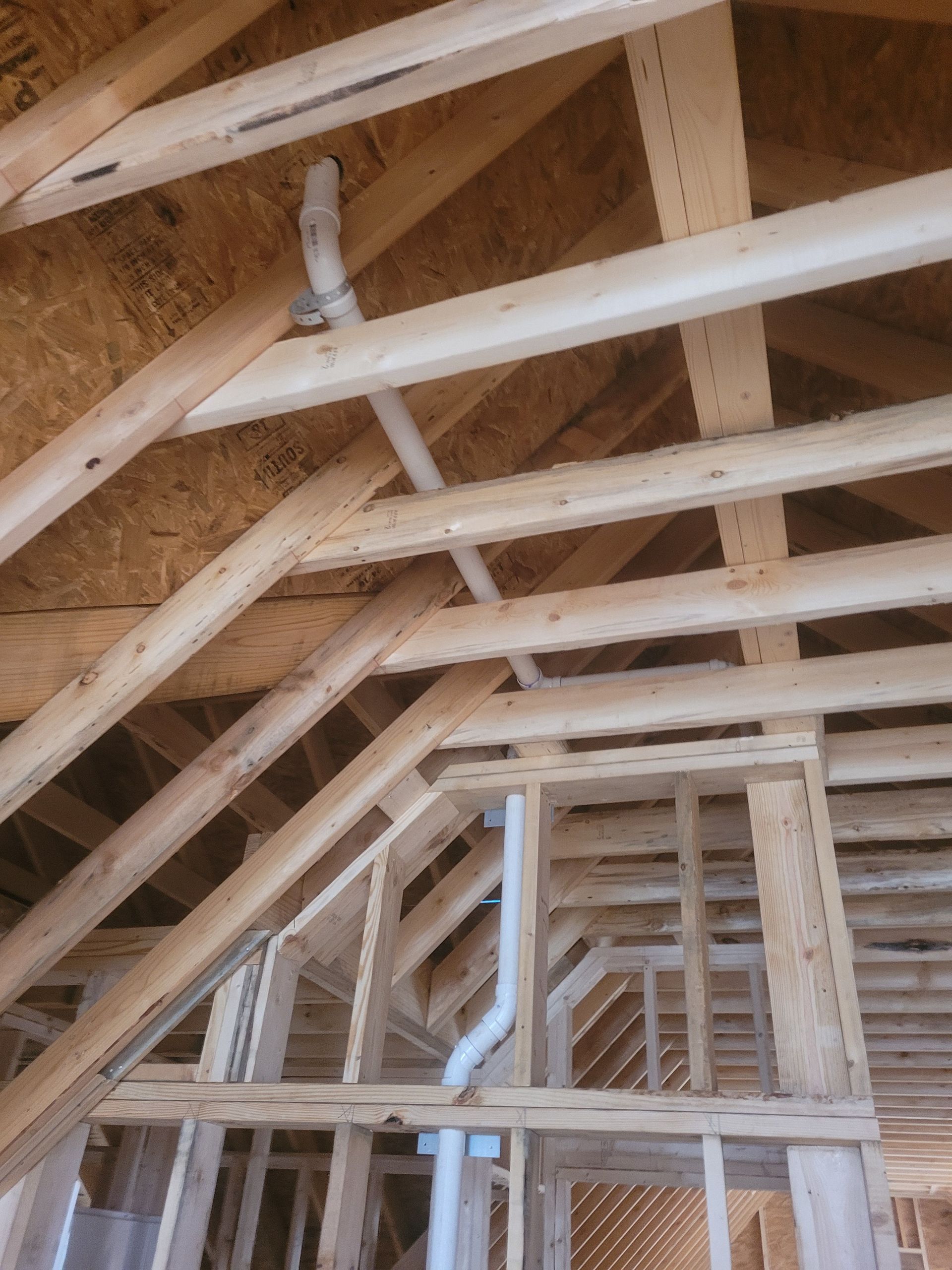 Wooden roof framing with white plumbing pipes, under construction.