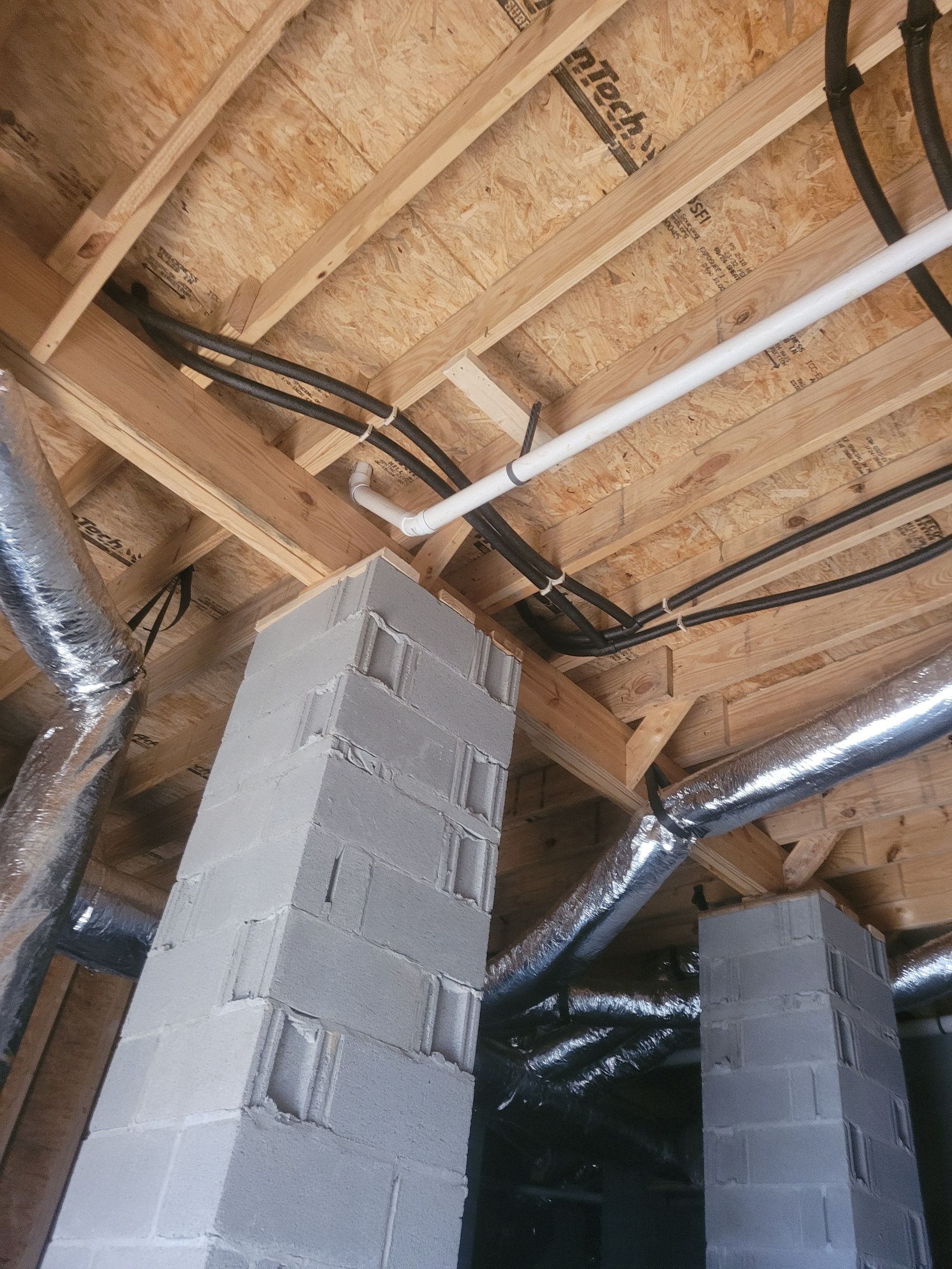 Looking up at exposed construction: cinder block pillars, wooden beams, ductwork, pipes.
