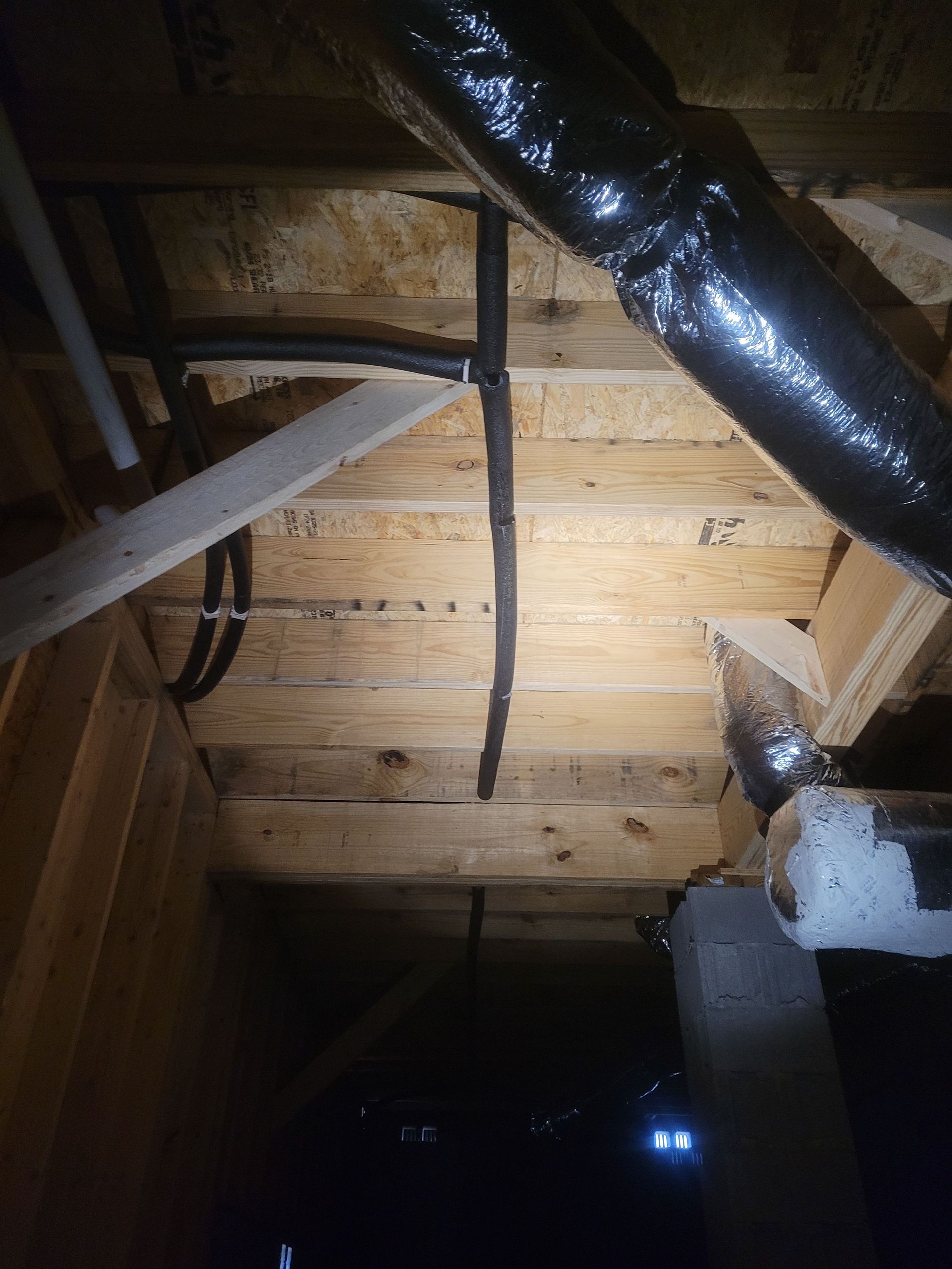 View from below of attic with wooden beams, dark wiring, and ductwork.